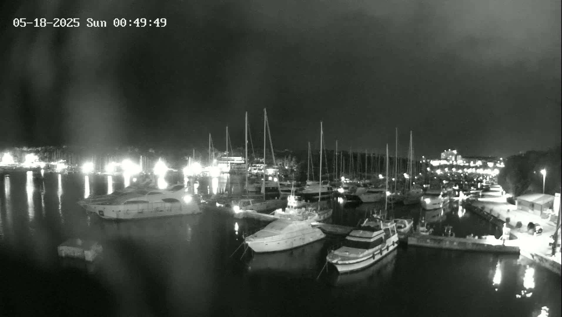 A marina at night with many boats docked, illuminated by lights on the shore under a dark sky.