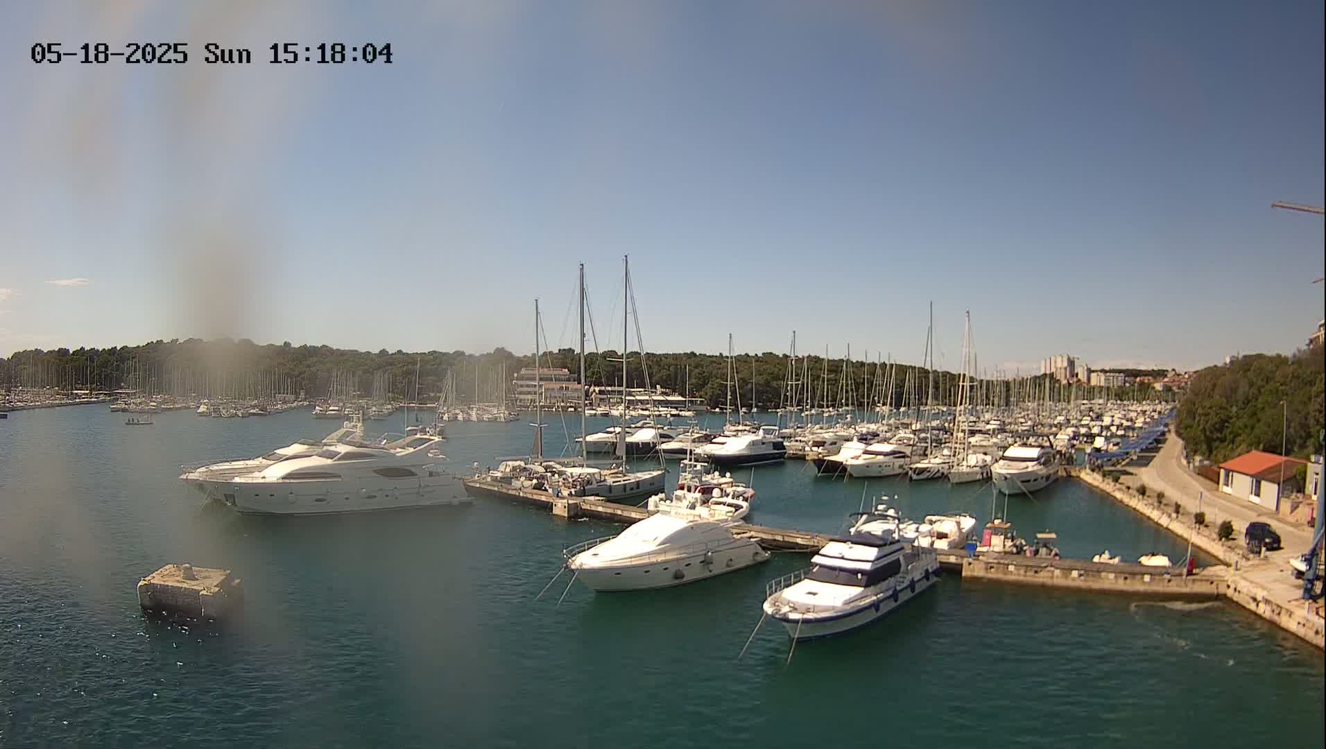 A sunny day shows a marina filled with numerous yachts and sailboats, docked along a pier with calm water.