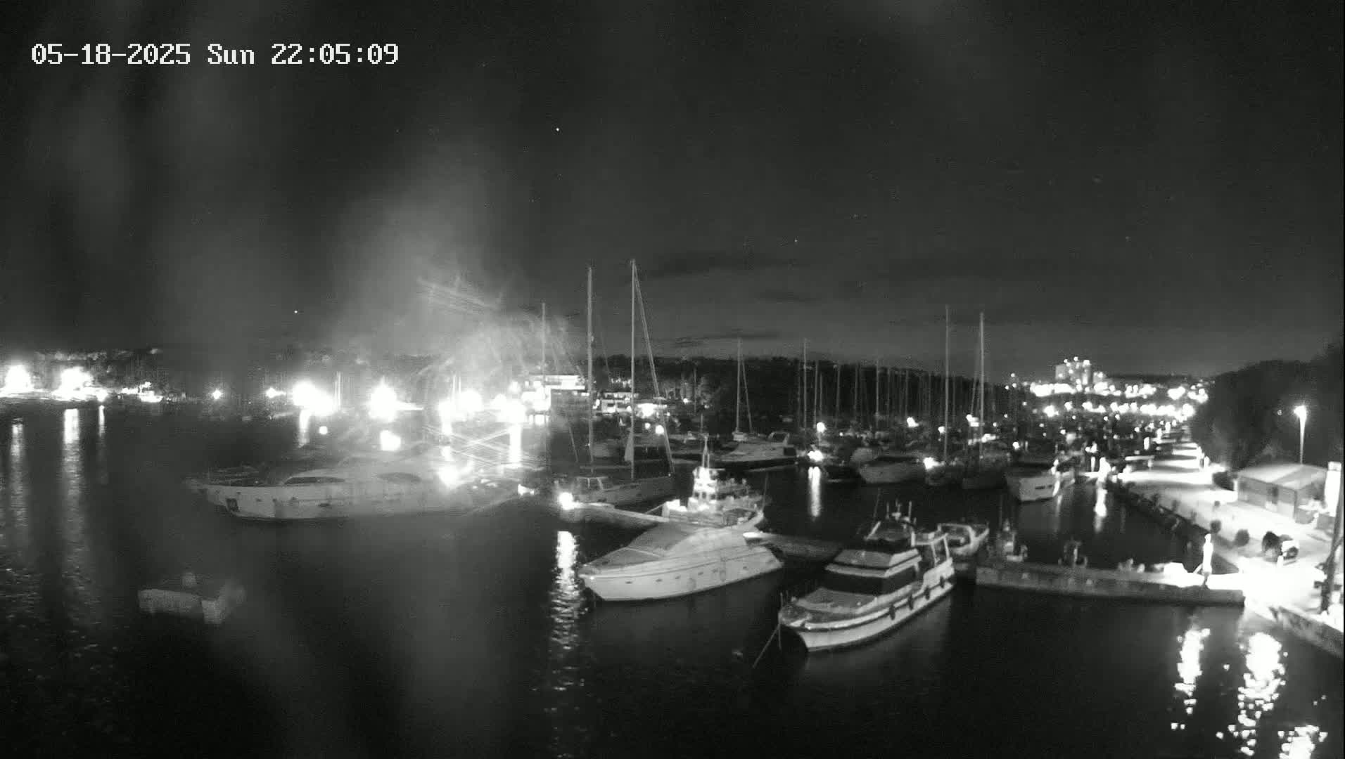 A nighttime, low-light view of a marina filled with numerous boats and yachts, under a mostly clear sky.