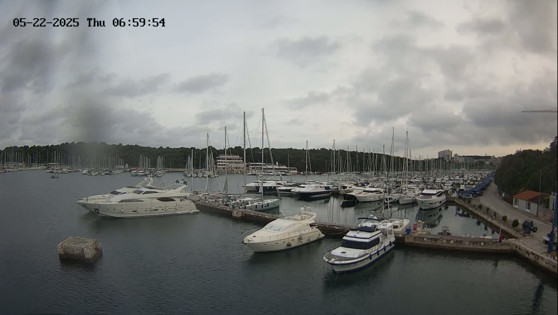 A marina filled with numerous sailboats and motor yachts under a cloudy sky.