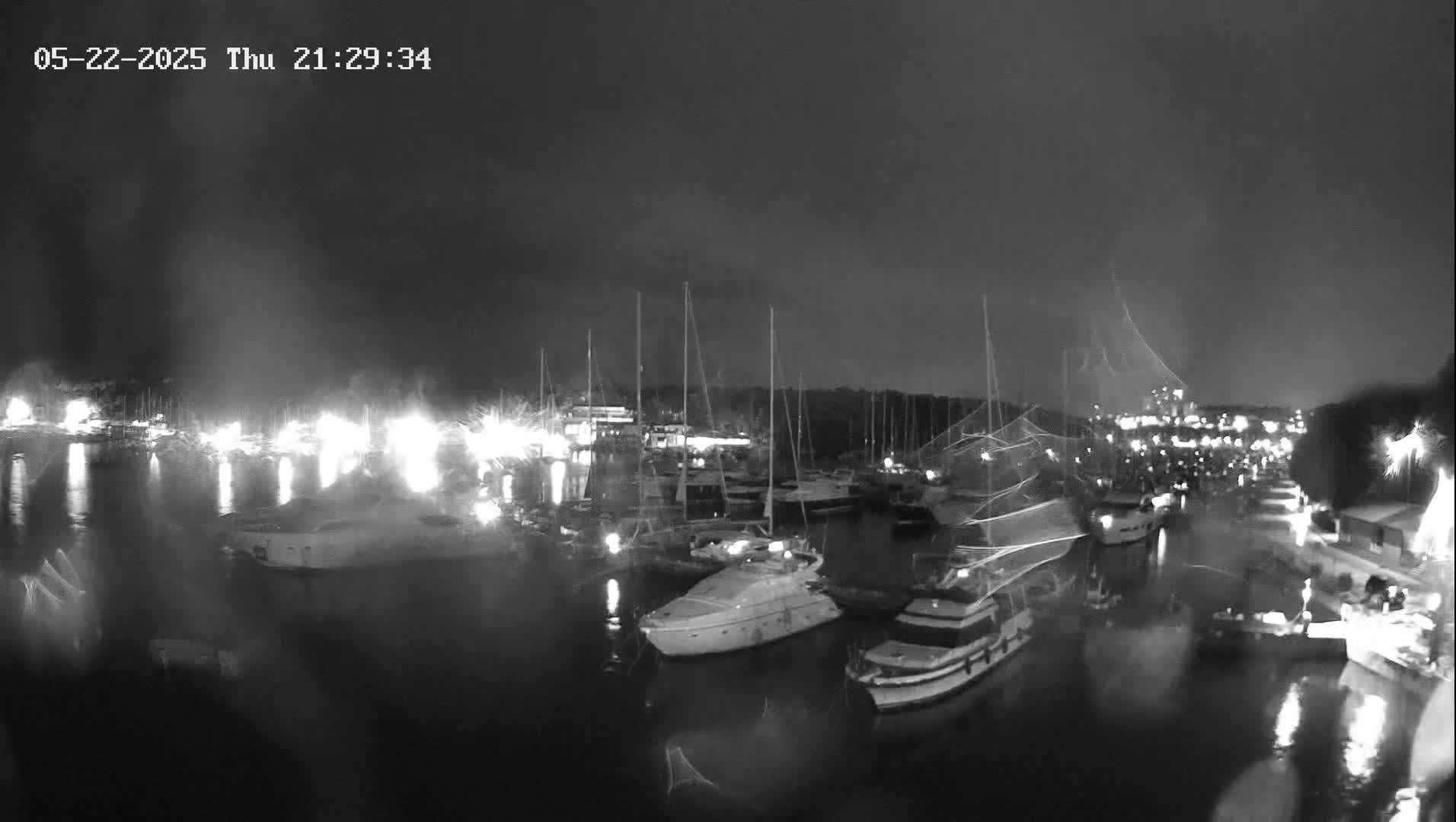 A nighttime, possibly rainy, view of a marina filled with boats and illuminated by lights.