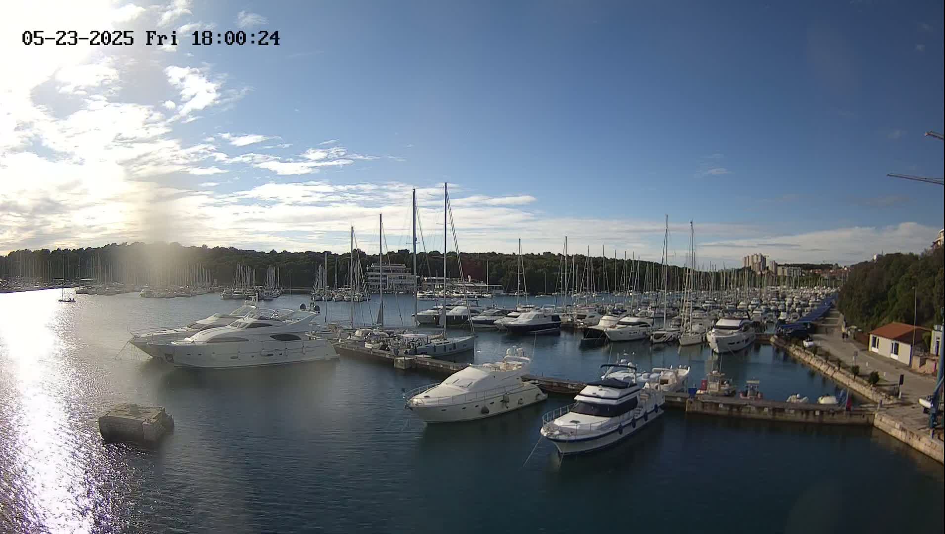 A marina filled with numerous yachts and sailboats is seen under a mostly sunny sky with some scattered clouds.