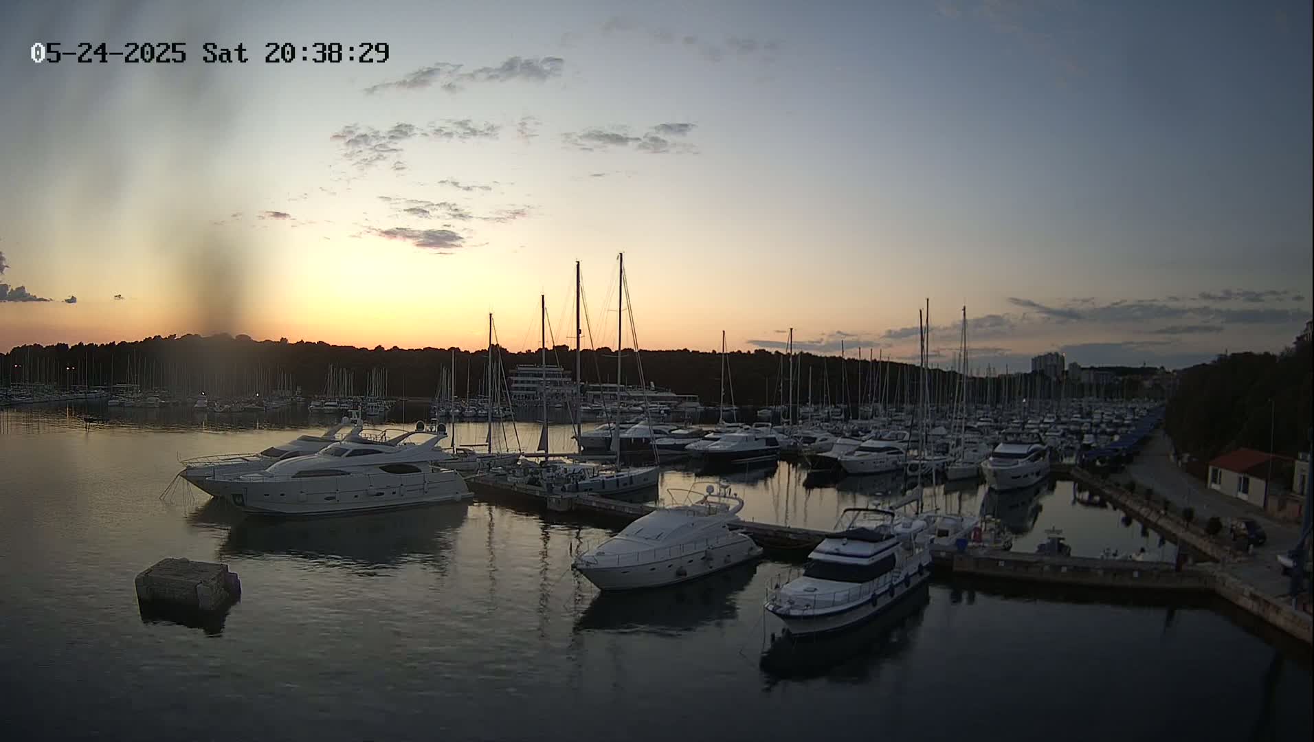 Many yachts and sailboats are docked in a marina at sunset under a partly cloudy sky.
