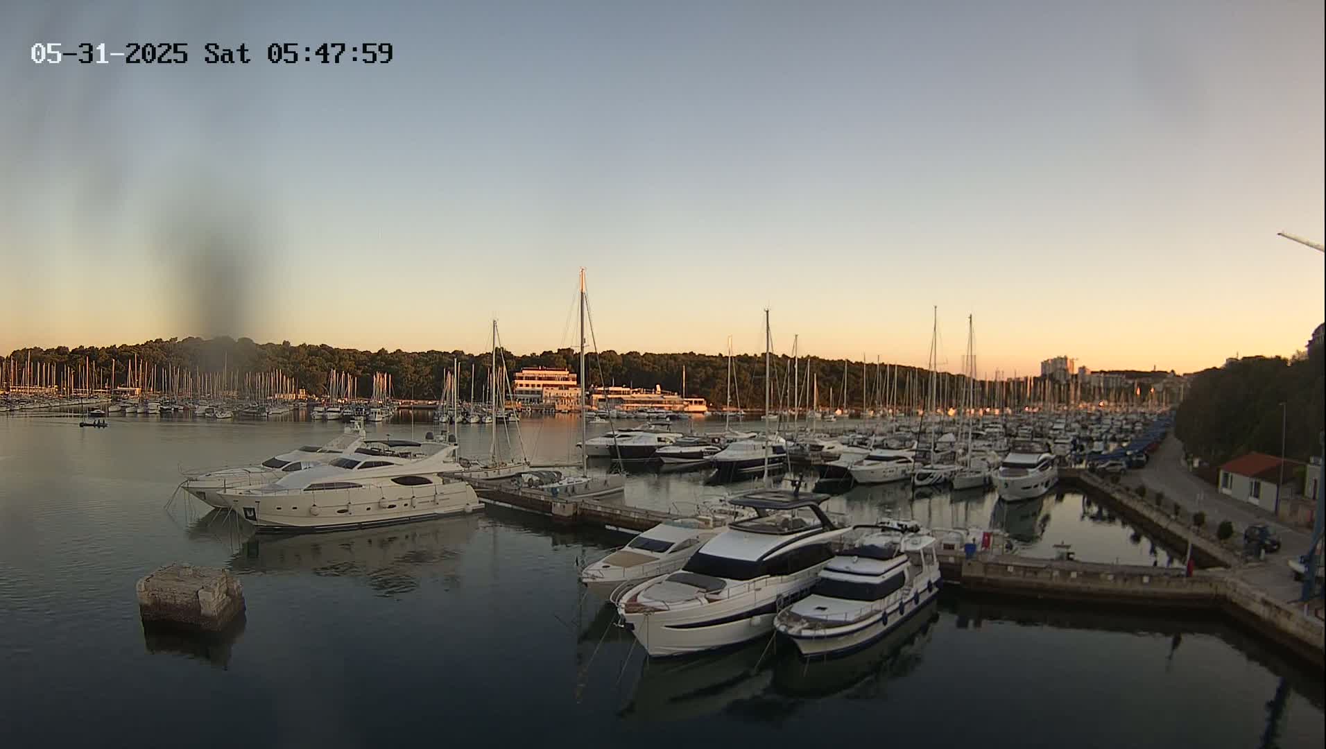 A marina filled with numerous sailboats and yachts at sunset under a clear sky.