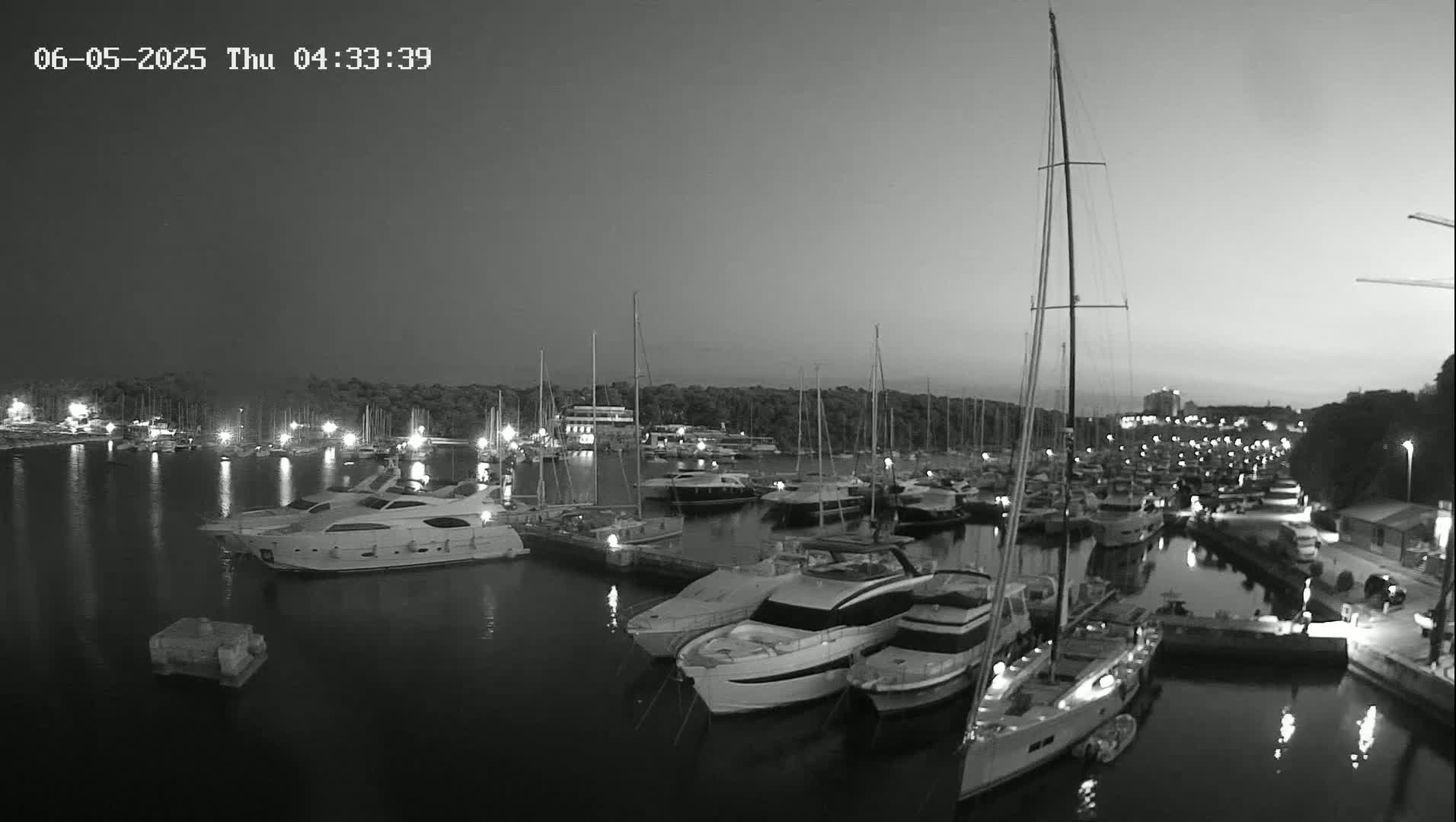 A marina filled with numerous yachts and sailboats is visible at twilight under a clear sky.