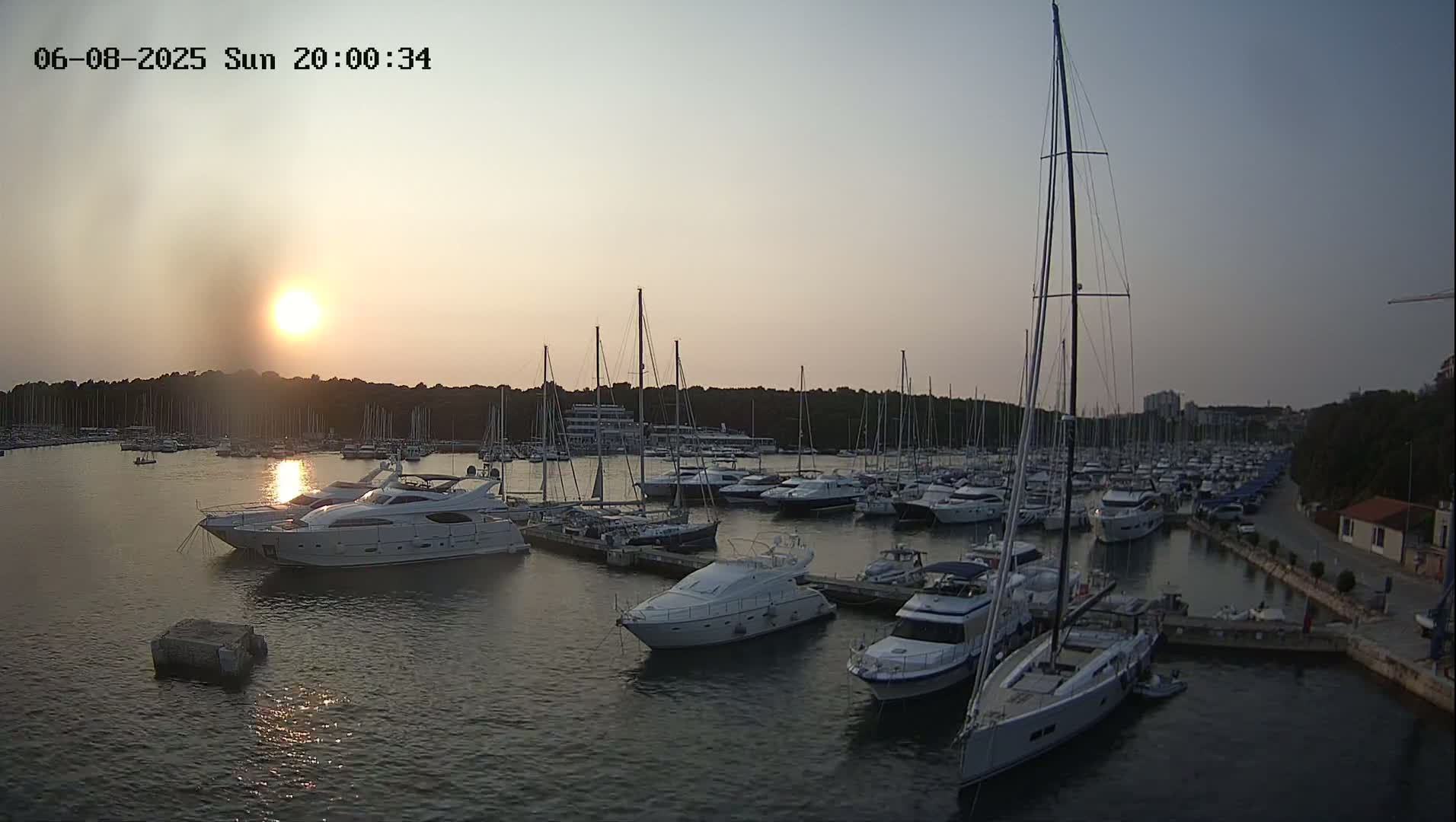 Many yachts and sailboats are docked in a marina at sunset under a clear sky.