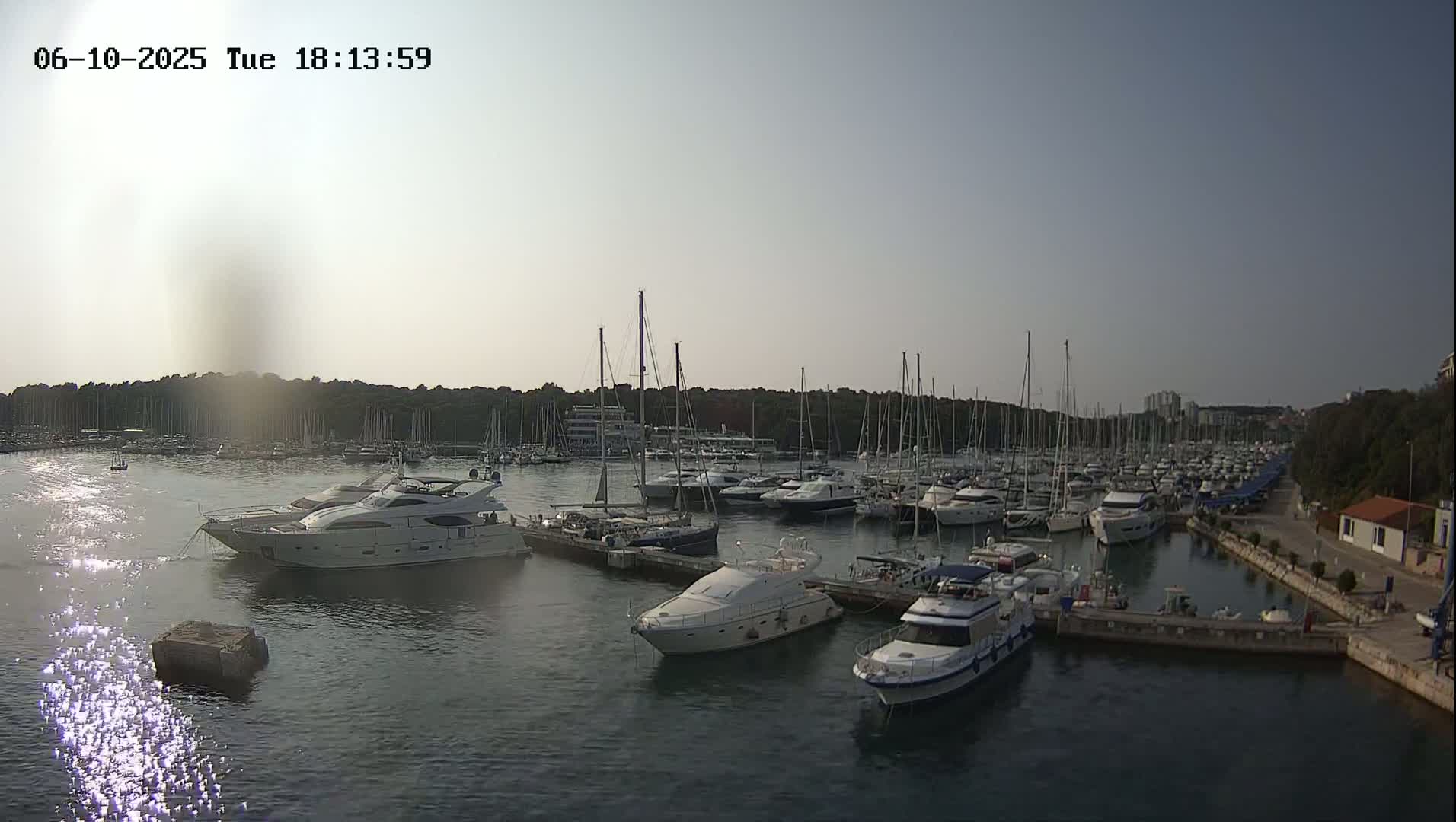 A marina filled with numerous sailboats and motor yachts is seen on a calm, sunny day.