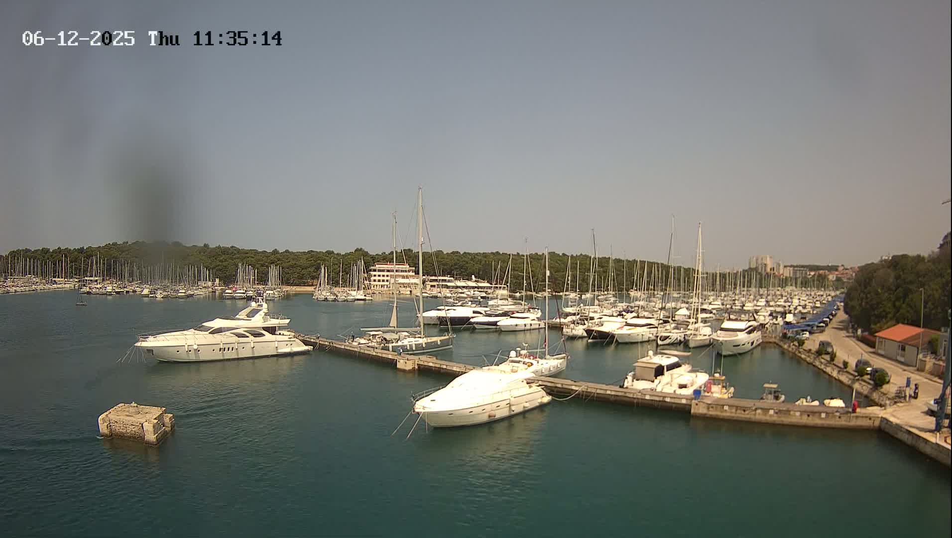 A marina filled with numerous sailboats and yachts is seen on a sunny day.