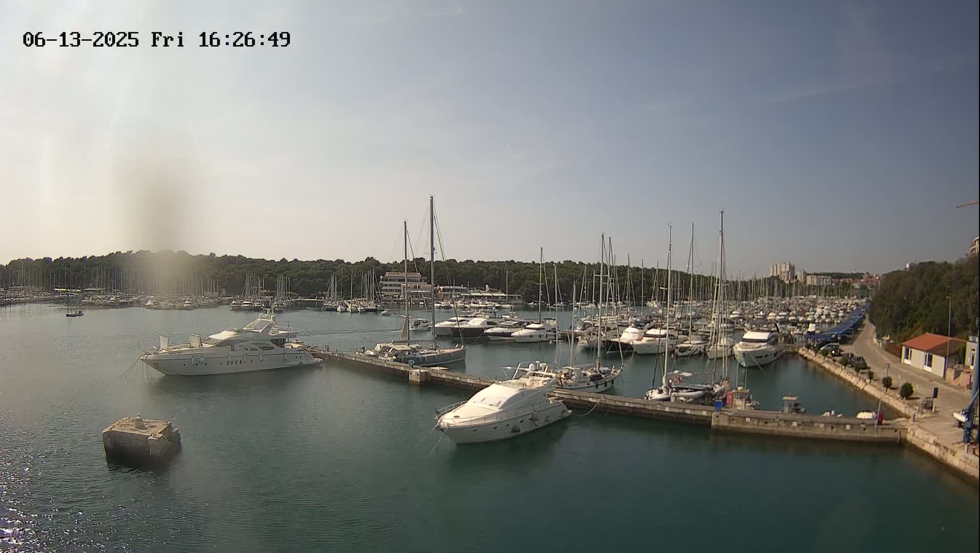 A marina filled with numerous sailboats and motor yachts is shown on a sunny day.