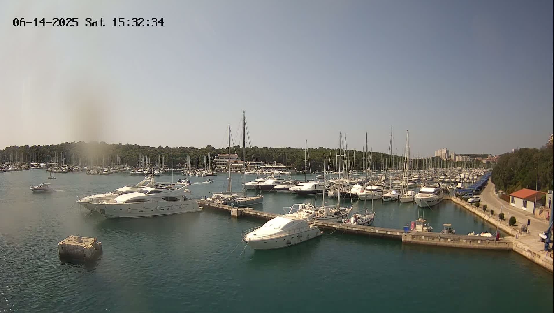 A marina filled with numerous sailboats and motor yachts is shown on a sunny day.
