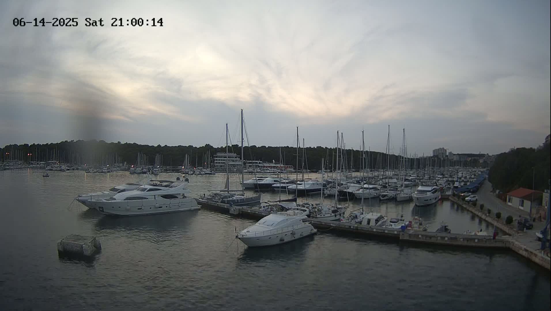 A marina filled with numerous sailboats and motor yachts is shown on a sunny day.