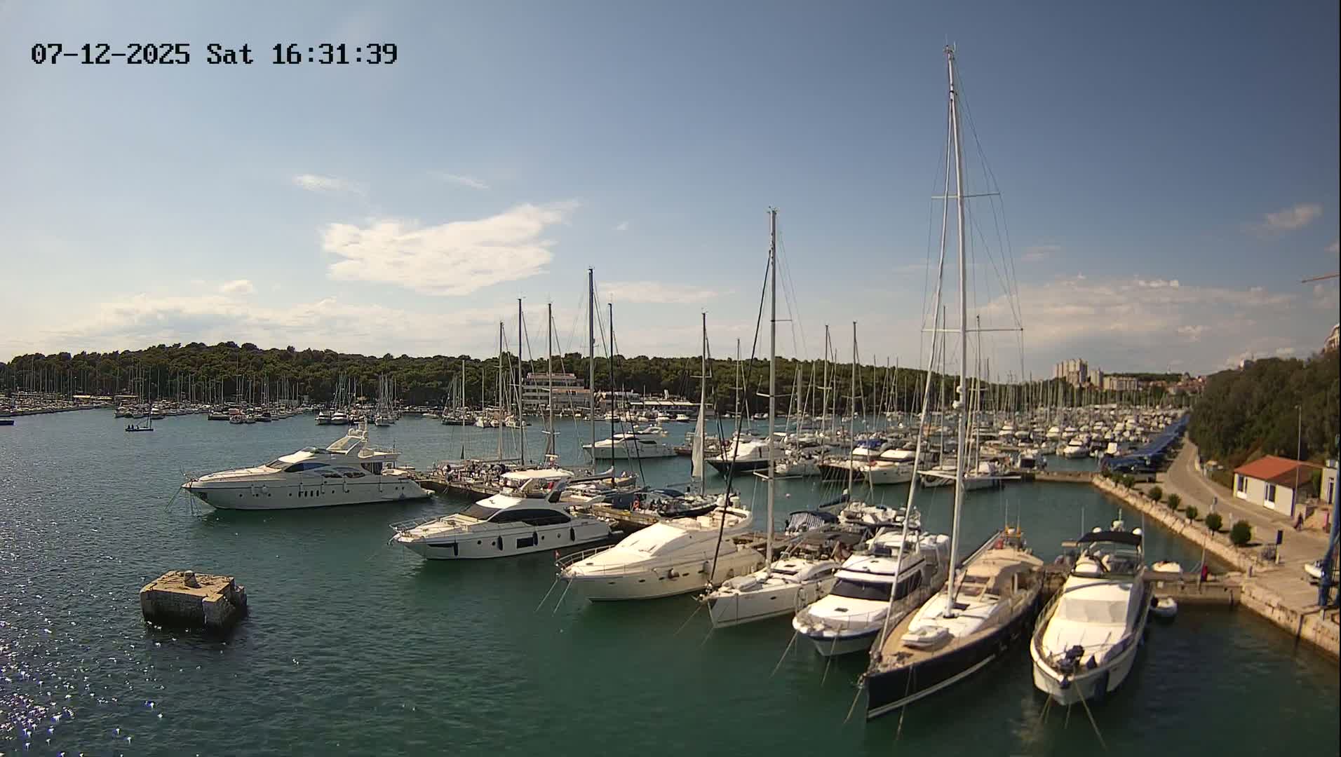 Many yachts and sailboats are docked in a marina on a sunny day.