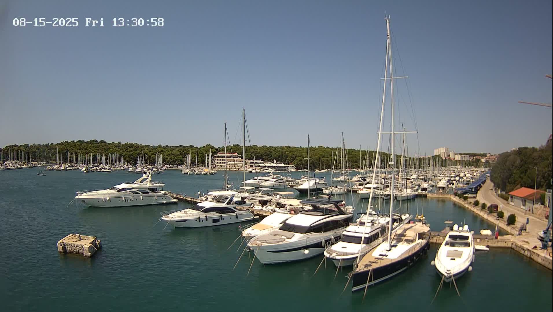 A marina filled with numerous yachts and sailboats is shown under a clear, sunny sky.