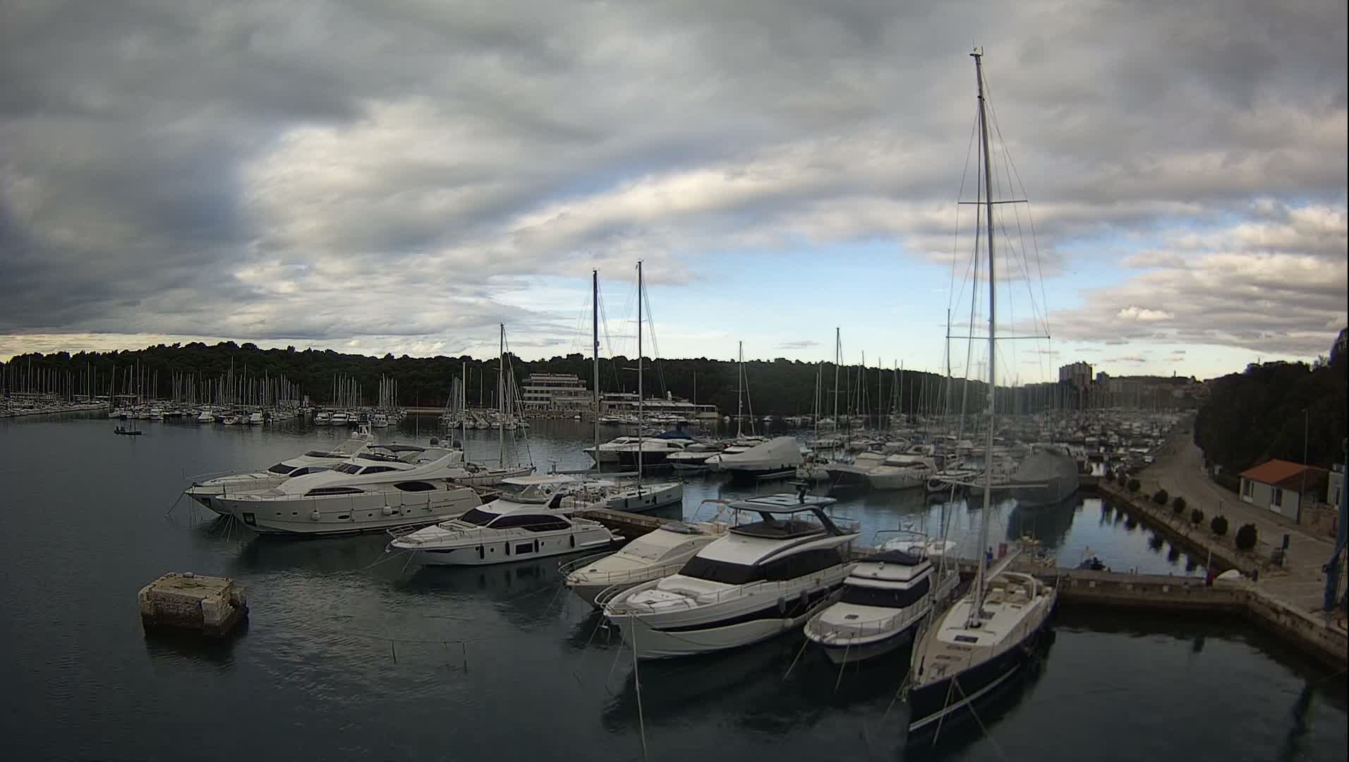 A marina filled with numerous yachts and sailboats is shown under a clear, sunny sky.