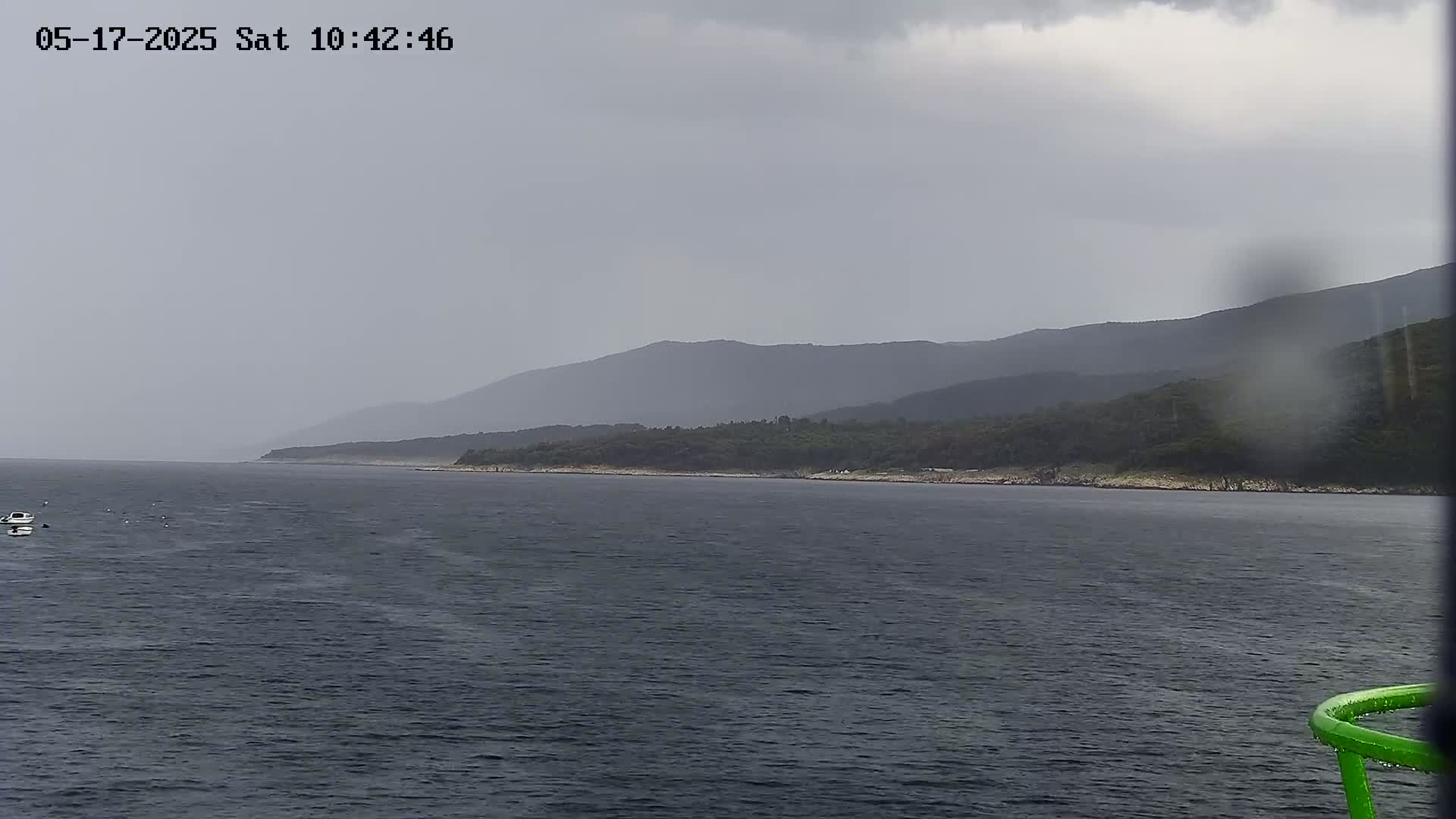 A view of a calm sea with a distant shoreline backed by hazy mountains under an overcast sky.