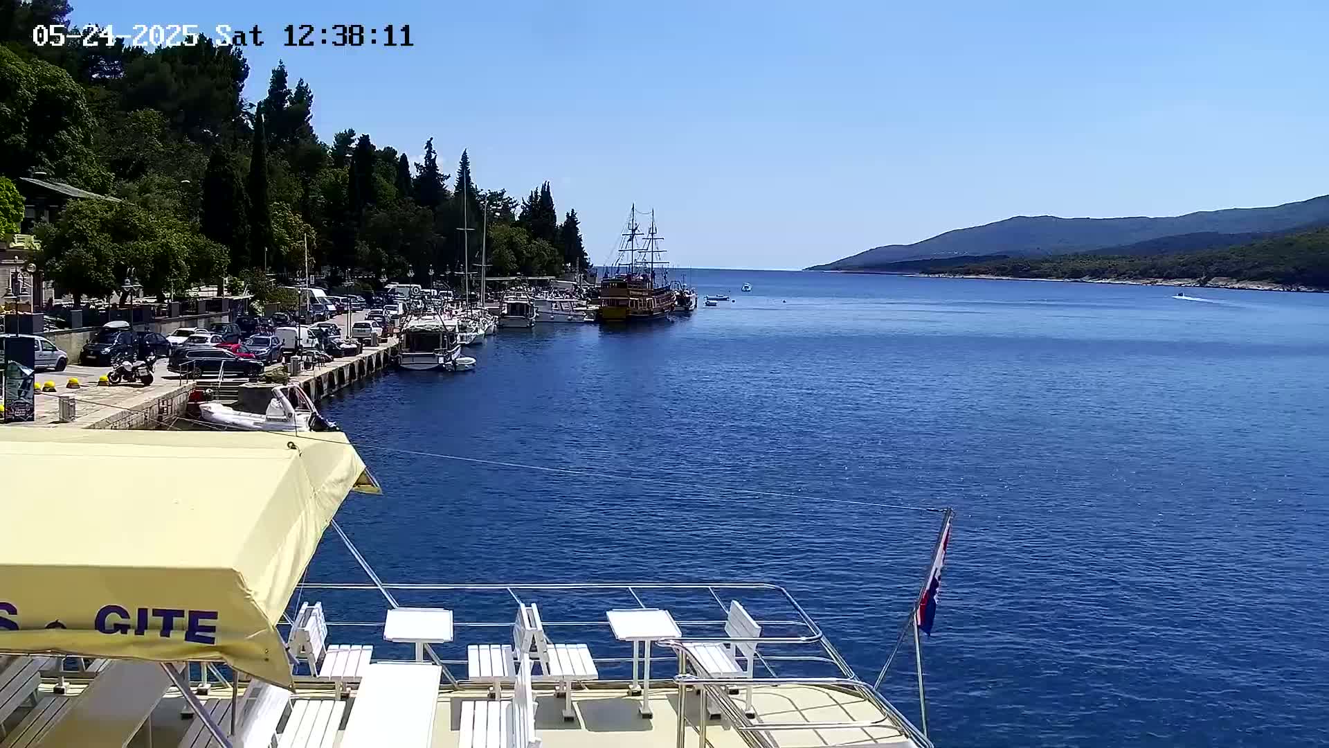 A harbor filled with boats and cars on a sunny day, viewed from the deck of a boat.