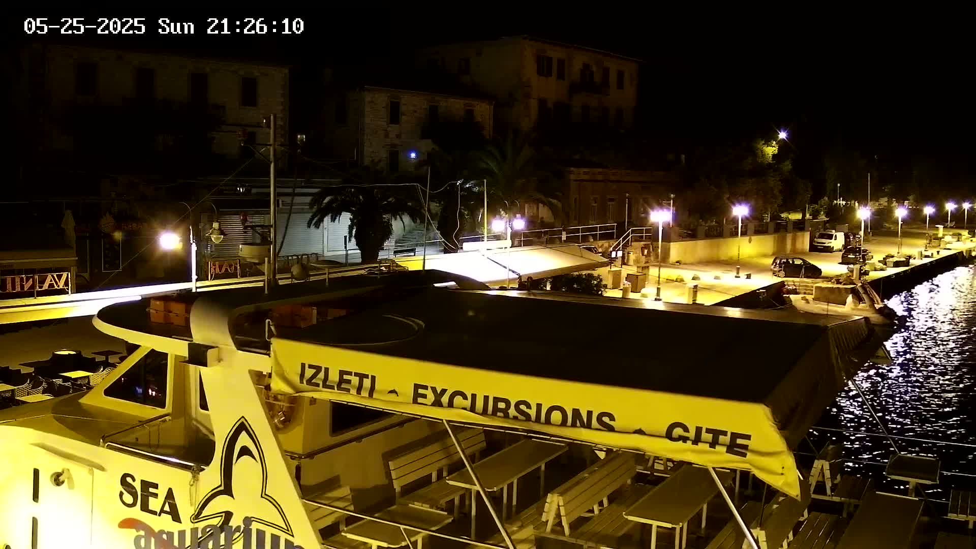 A yellow excursion boat is docked at night next to a waterfront illuminated by streetlights, with several cars parked nearby.