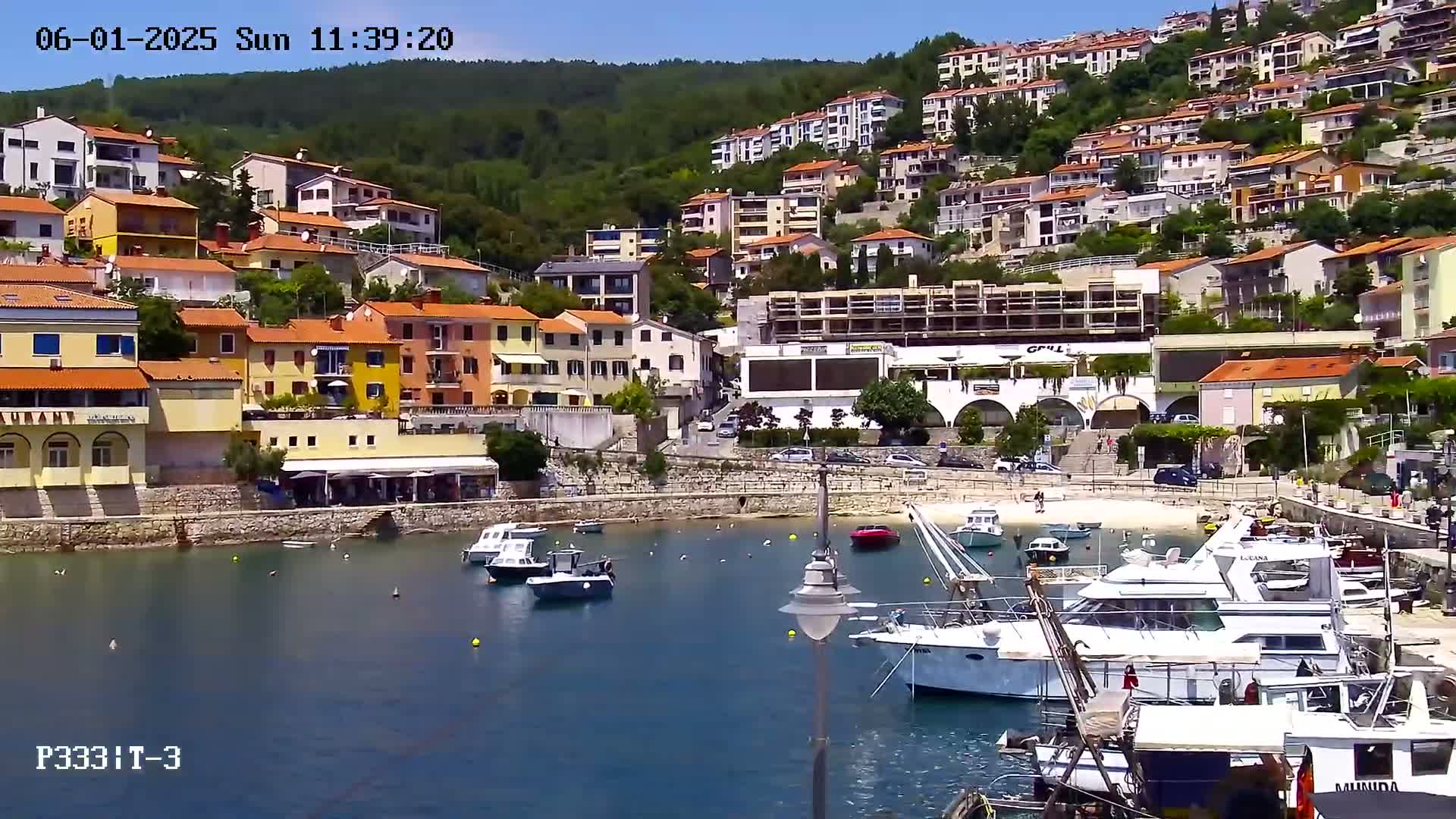A sunny day shows a small harbor filled with boats, nestled next to a hillside town of colorful buildings.