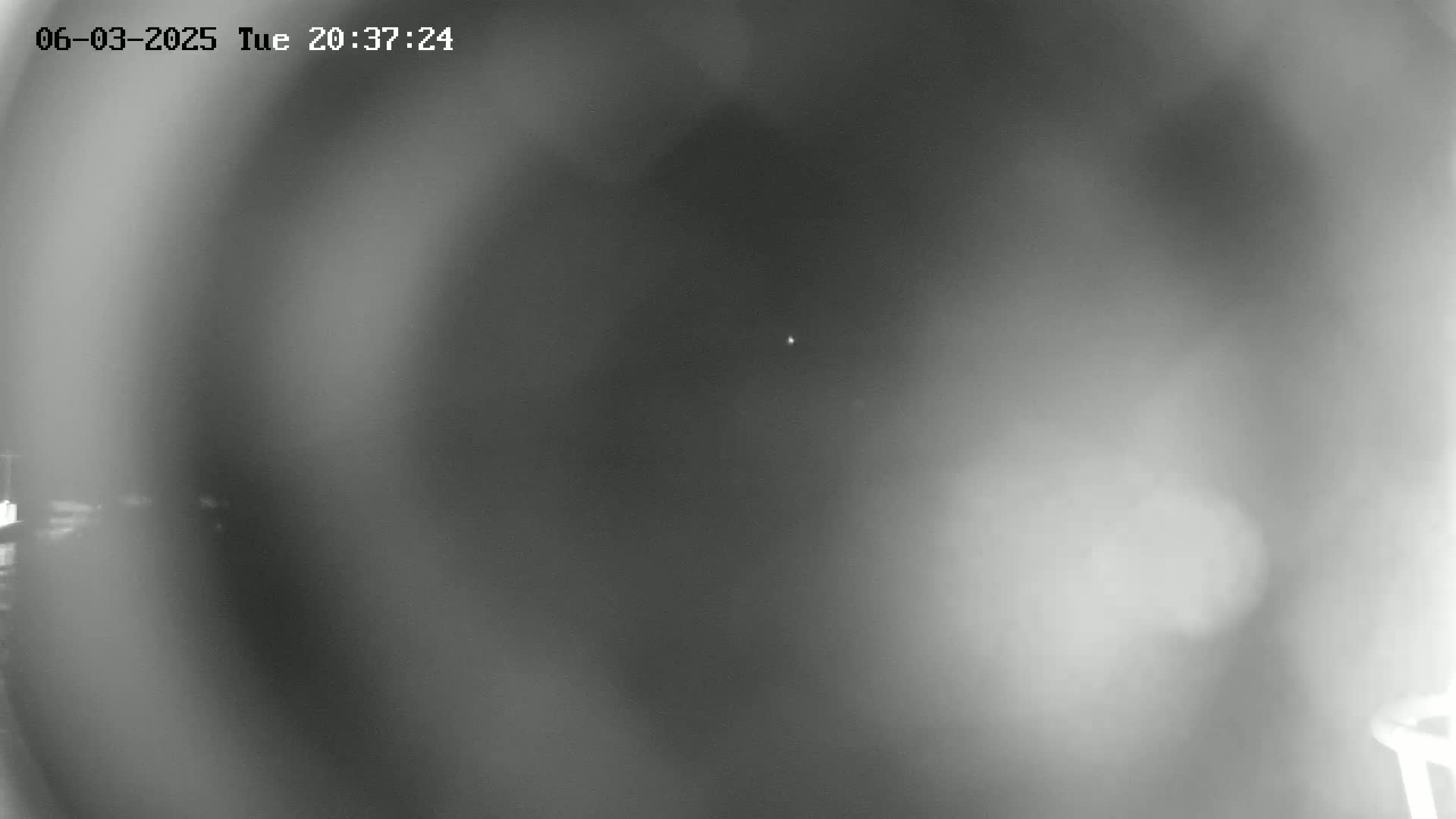 A blurry, grayscale nighttime image shows a faint light in the distance under hazy or foggy conditions.