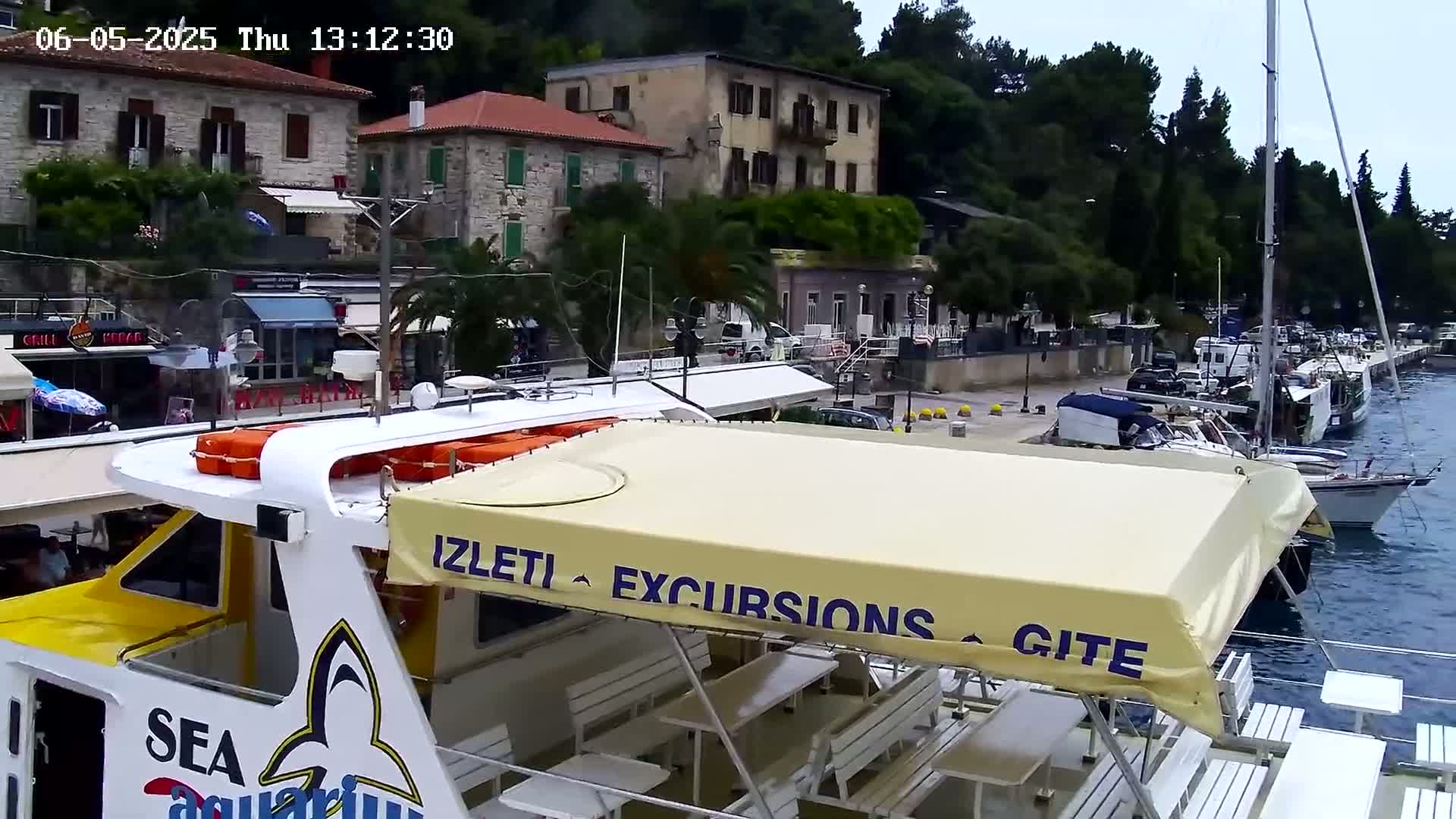 A yellow and white excursion boat with a beige awning is docked at a harbor beside stone buildings and numerous other boats under an overcast sky.