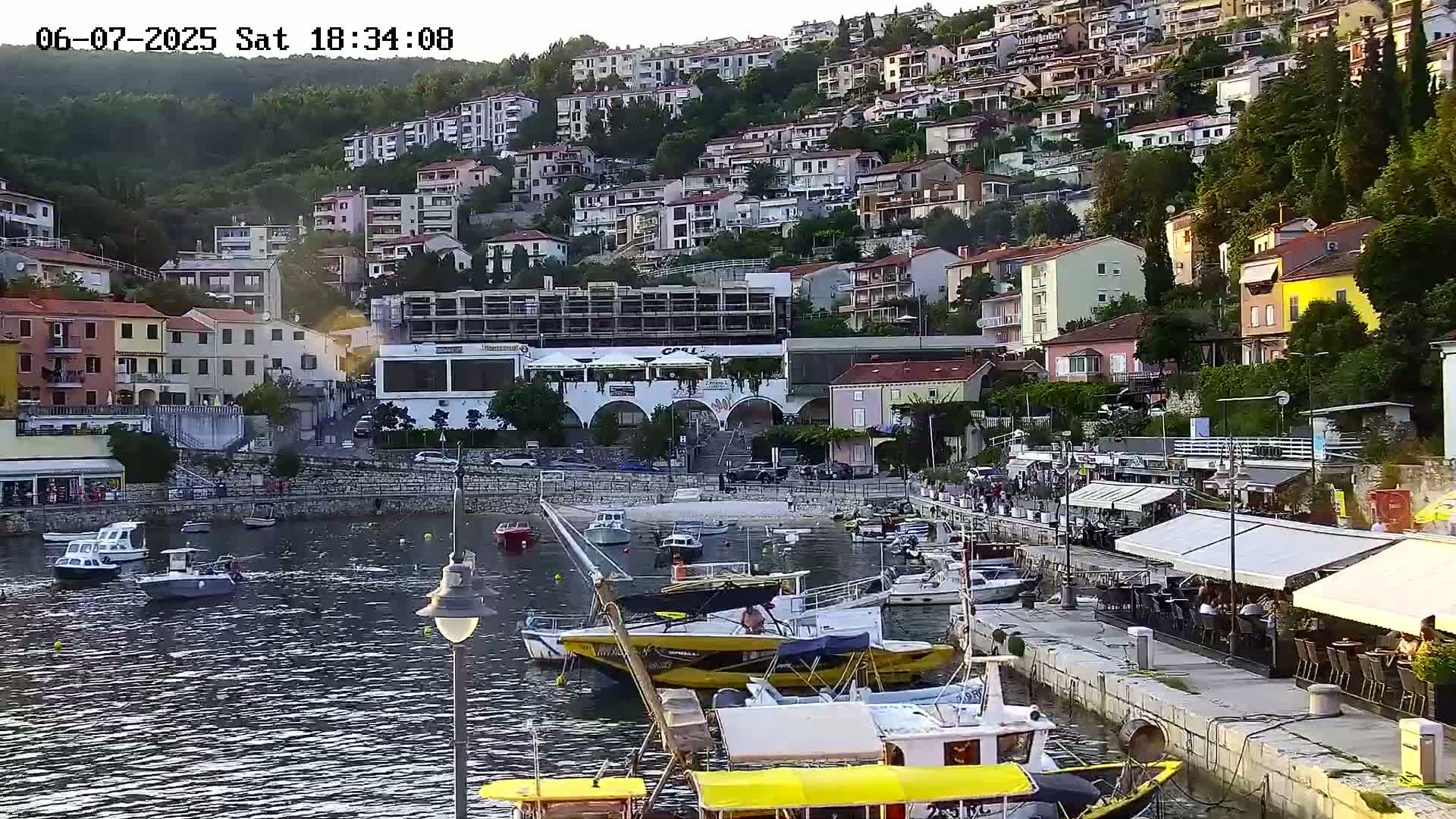 A harbor filled with boats is nestled beside a hillside town at sunset.