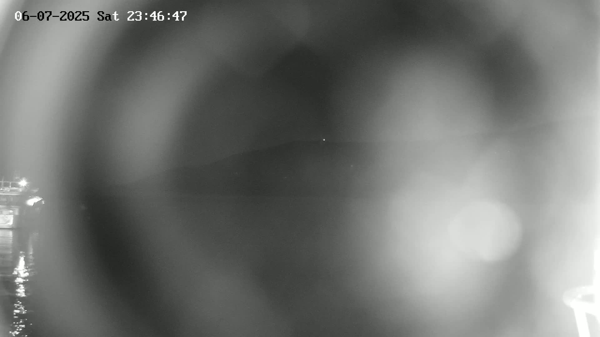 A blurry nighttime image shows a dark body of water with a distant, indistinct shoreline and a small, indistinct vessel on the left.