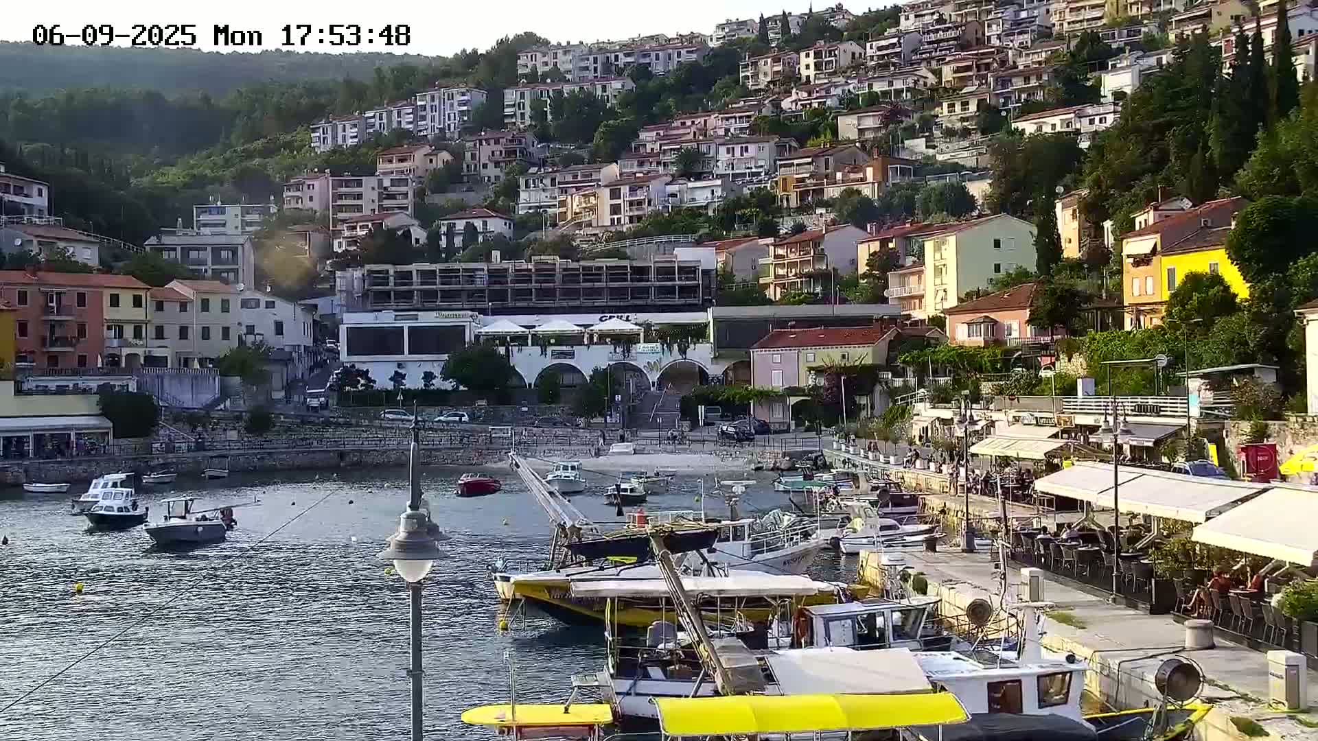 A harbor filled with boats sits below a hillside town under a mostly clear evening sky.