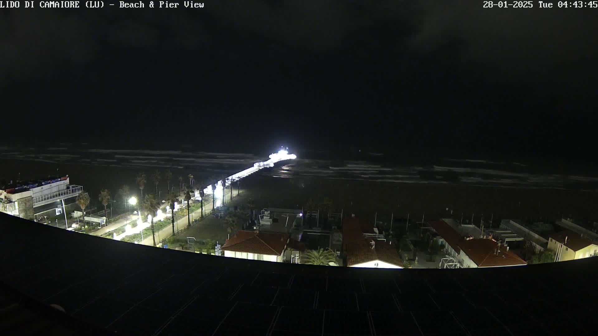 A nighttime view of a beach and pier with lightly-choppy waves under a dark sky.