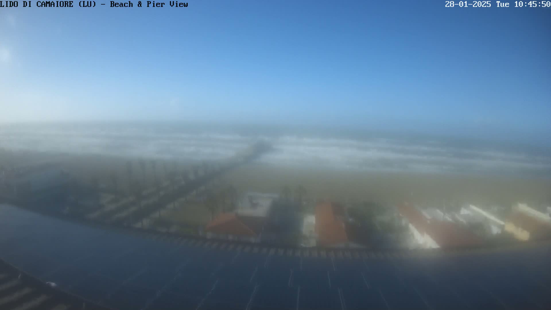 A hazy, foggy view of a beach, pier, and buildings under a clear blue sky.