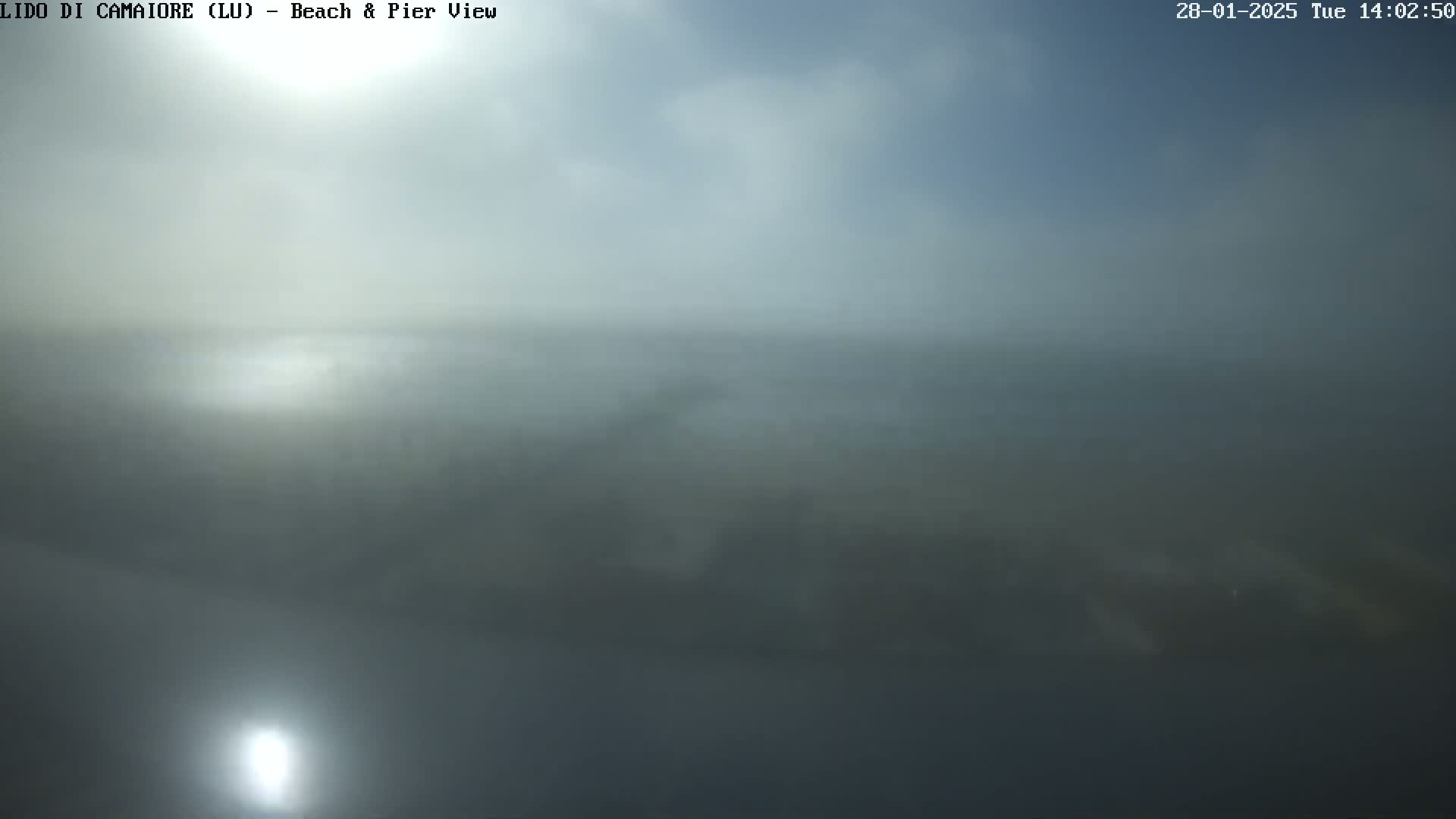 A hazy, overcast view of a beach and pier is visible from a distance, with the sun reflecting on the water.