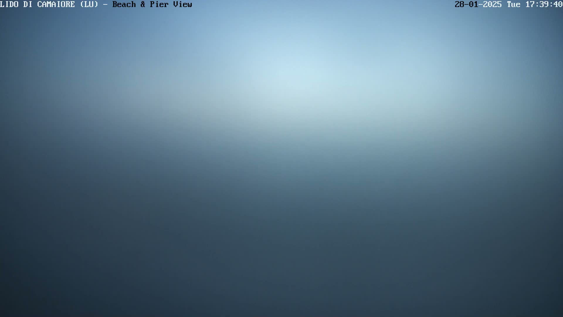A blurry, hazy, blue image shows an overcast sky over a beach and pier.