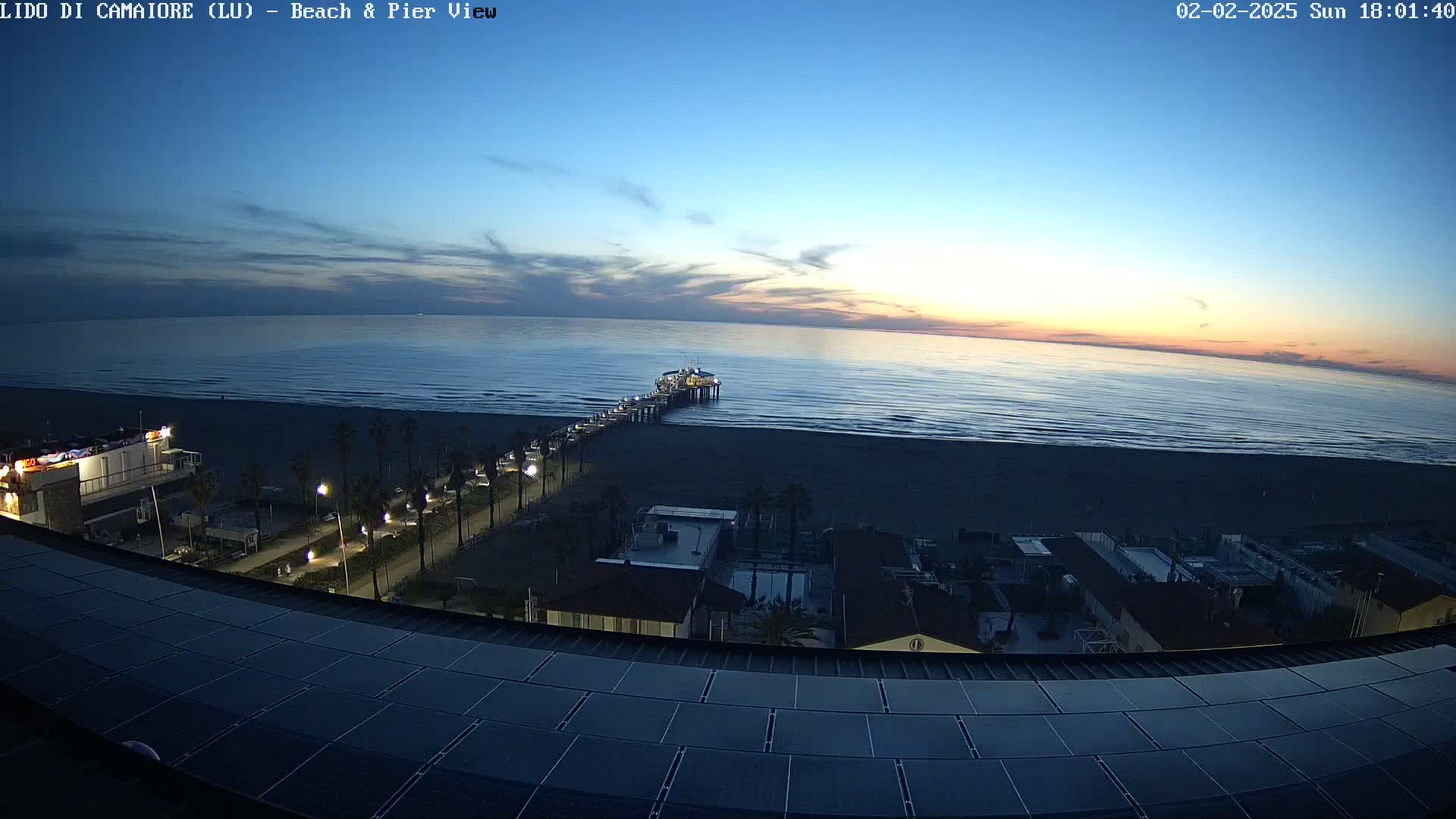 A long pier extends from a beach into a calm ocean under a twilight sky.