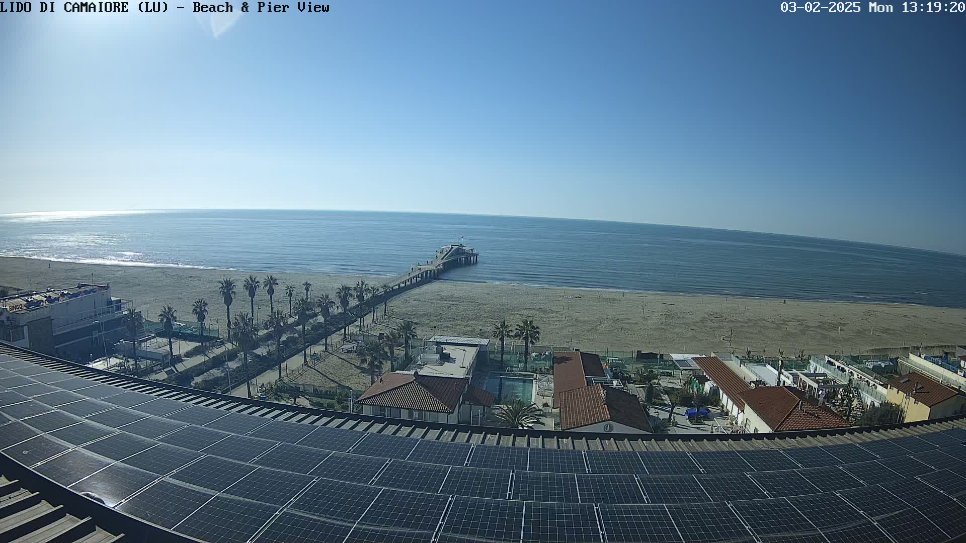 A long pier extends from a sandy beach into a calm ocean under a clear blue sky.