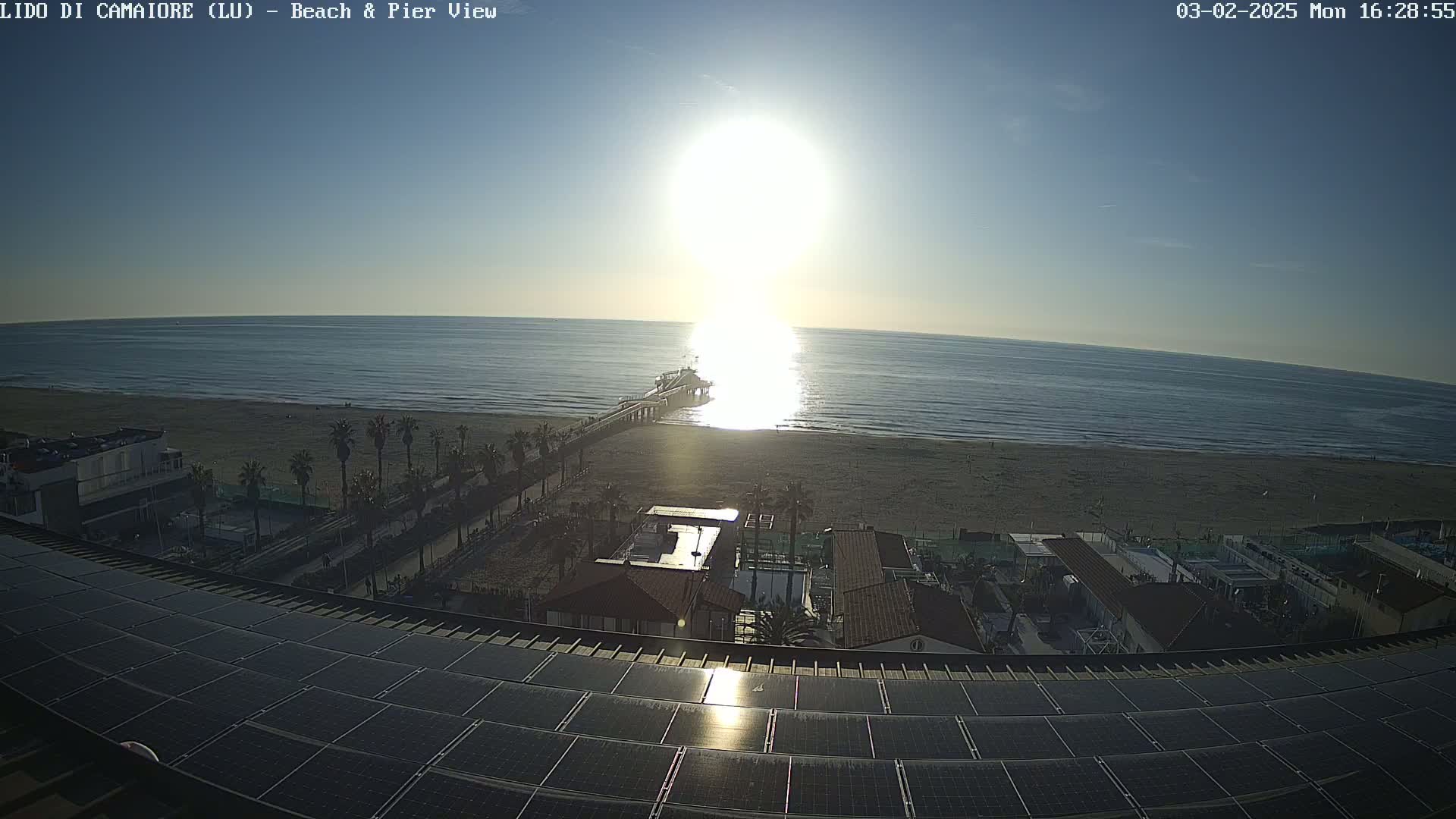 A sunny day overlooking a beach, pier, and buildings with a solar panel array in the foreground.