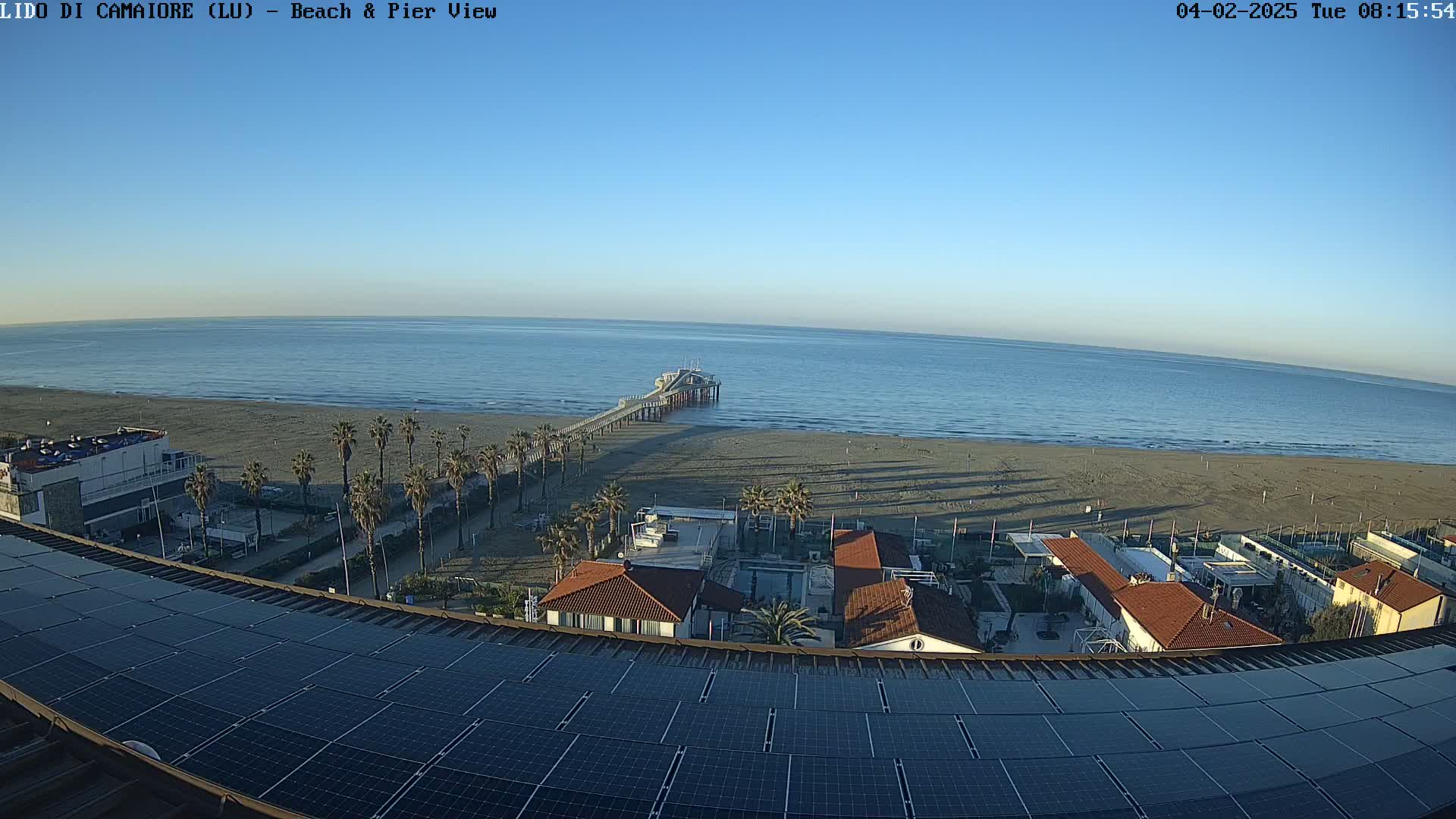 A long pier extends from a sandy beach into a calm ocean under a clear blue sky.
