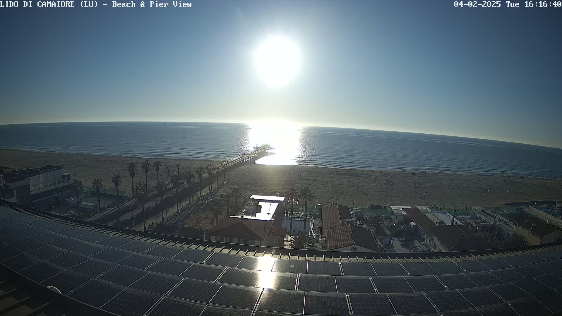 A sunny day overlooking a beach, pier, and ocean from a rooftop with solar panels.