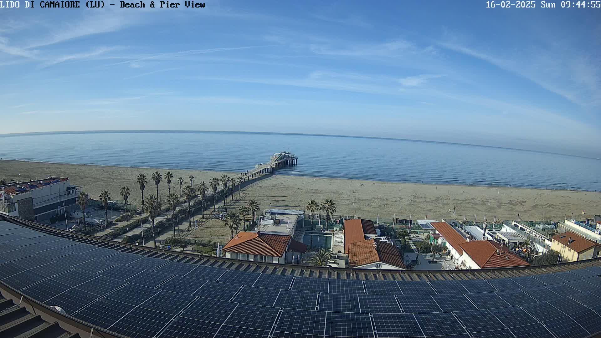 A long pier extends from a sandy beach into a calm ocean under a mostly clear sky.
