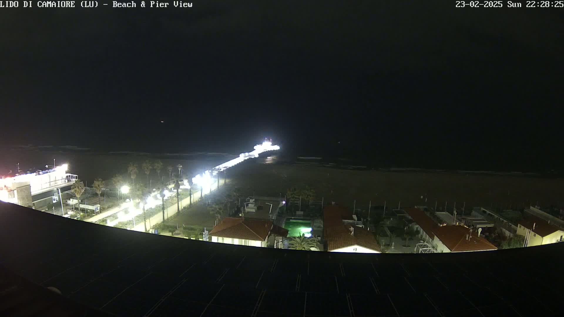 A nighttime view of a beach and pier, with a dark sky and calm ocean.