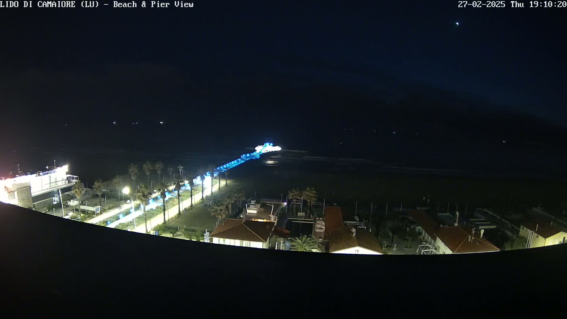 A nighttime view of a beach and pier, illuminated with blue lights, under a dark sky.