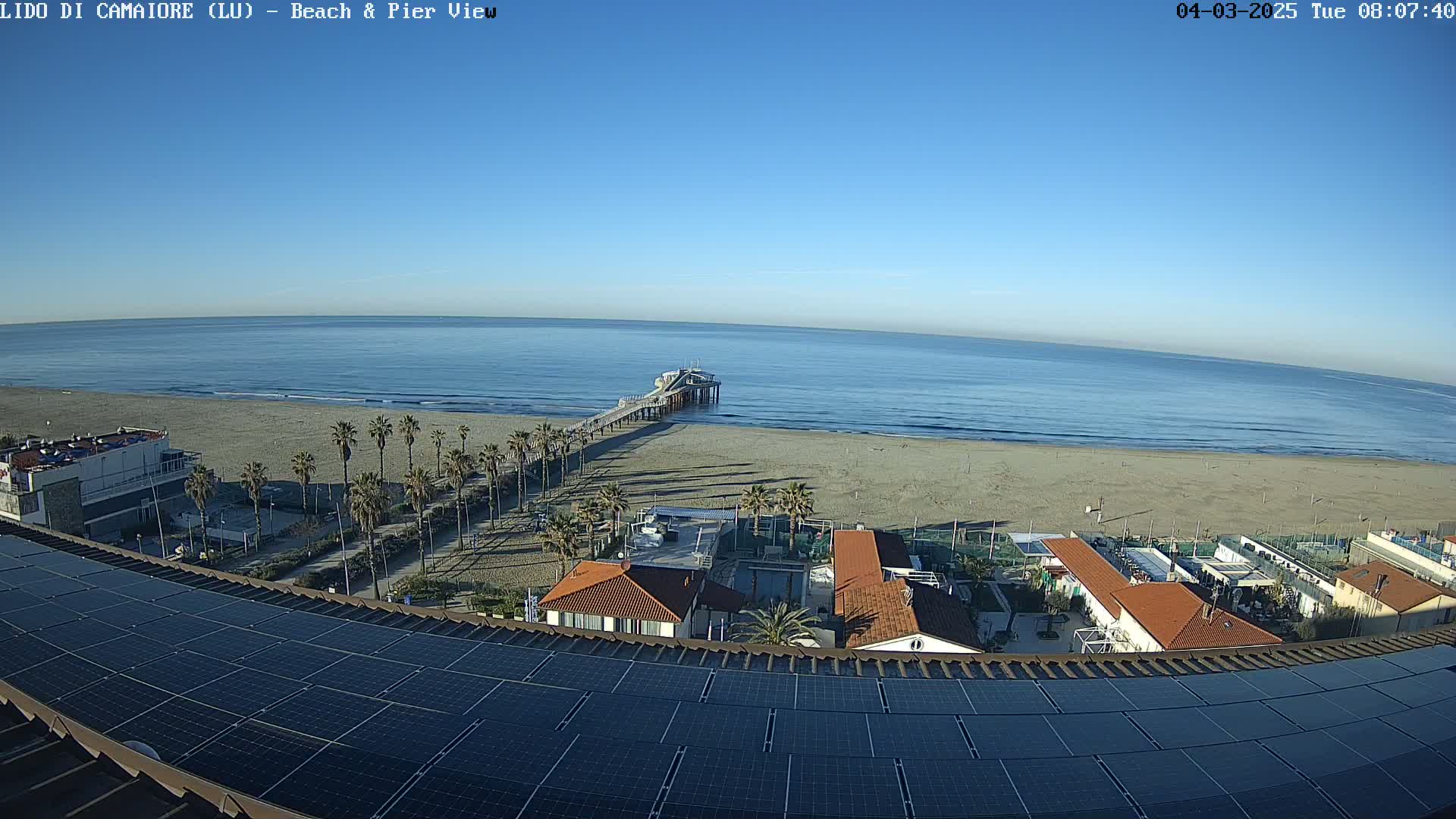 A long pier extends from a sandy beach into a calm ocean under a clear blue sky.