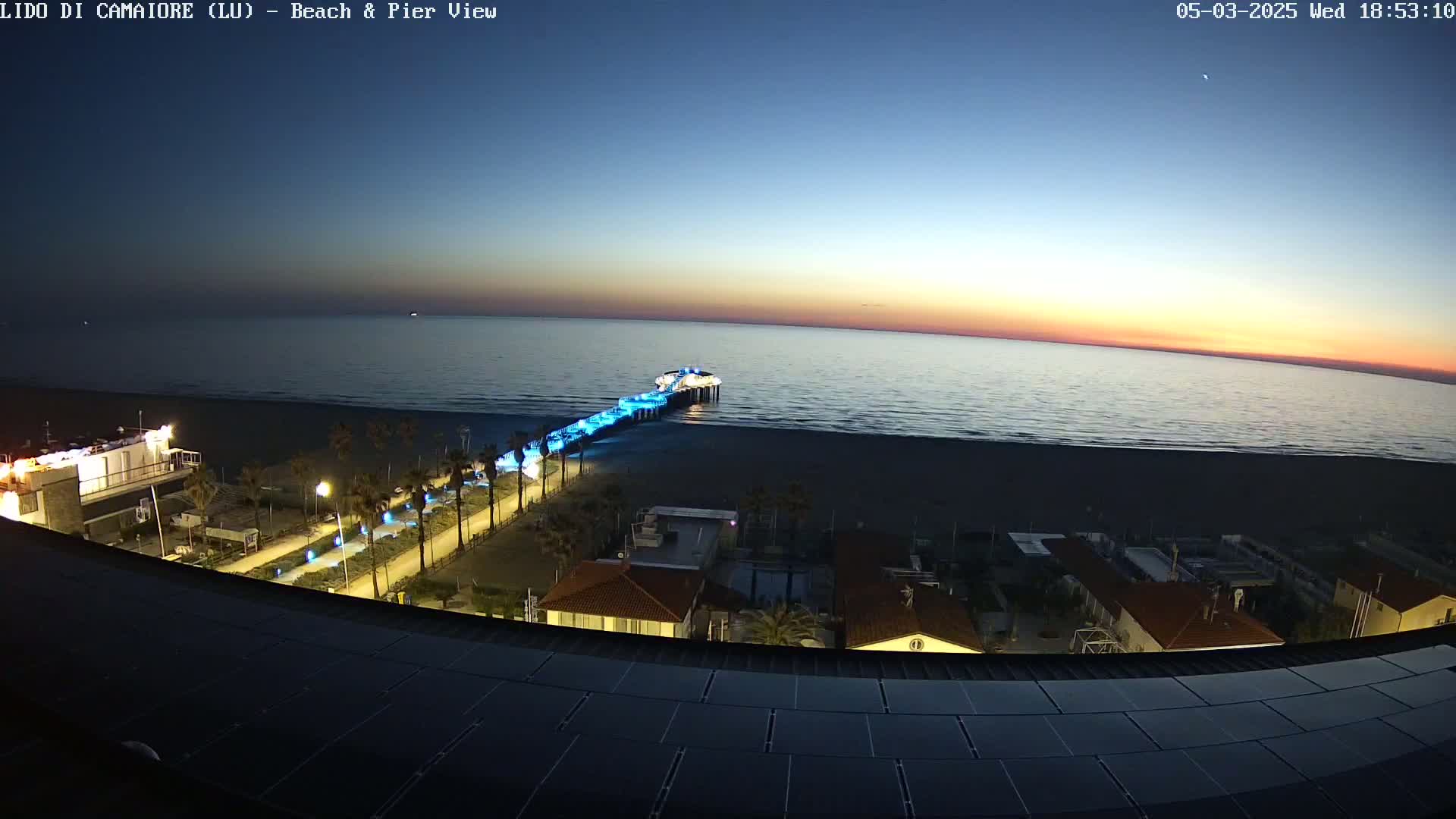 An illuminated pier extends from a beach into a calm ocean under a twilight sky.