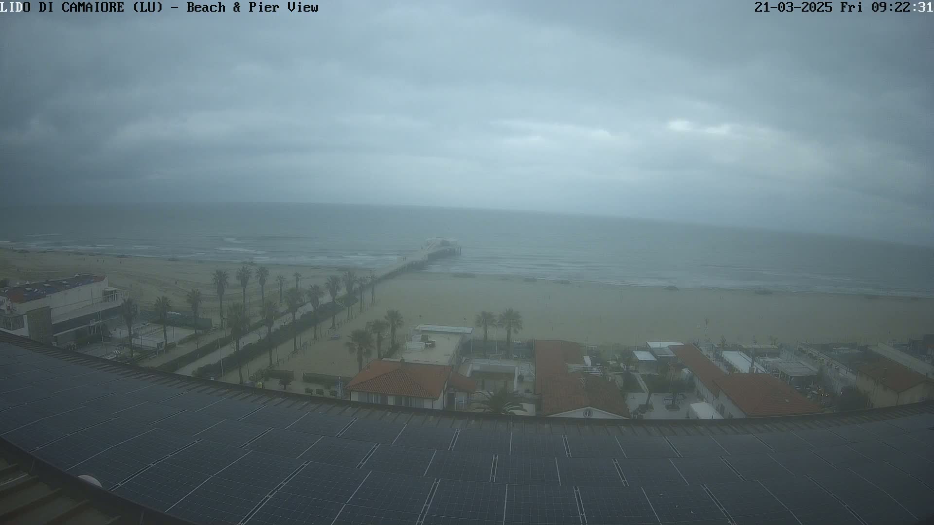 A view from above shows a beach, pier, and buildings on an overcast day with a gray sky and somewhat choppy ocean.