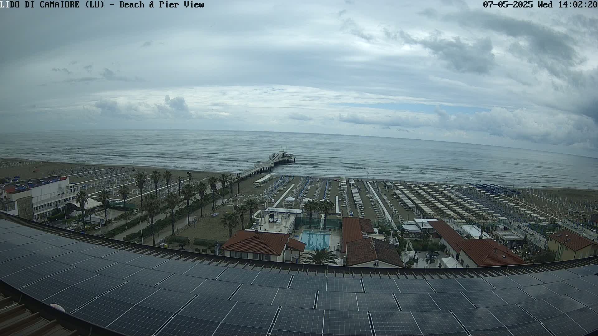 A beach with rows of umbrellas and a pier extends into a somewhat choppy sea under a cloudy sky.