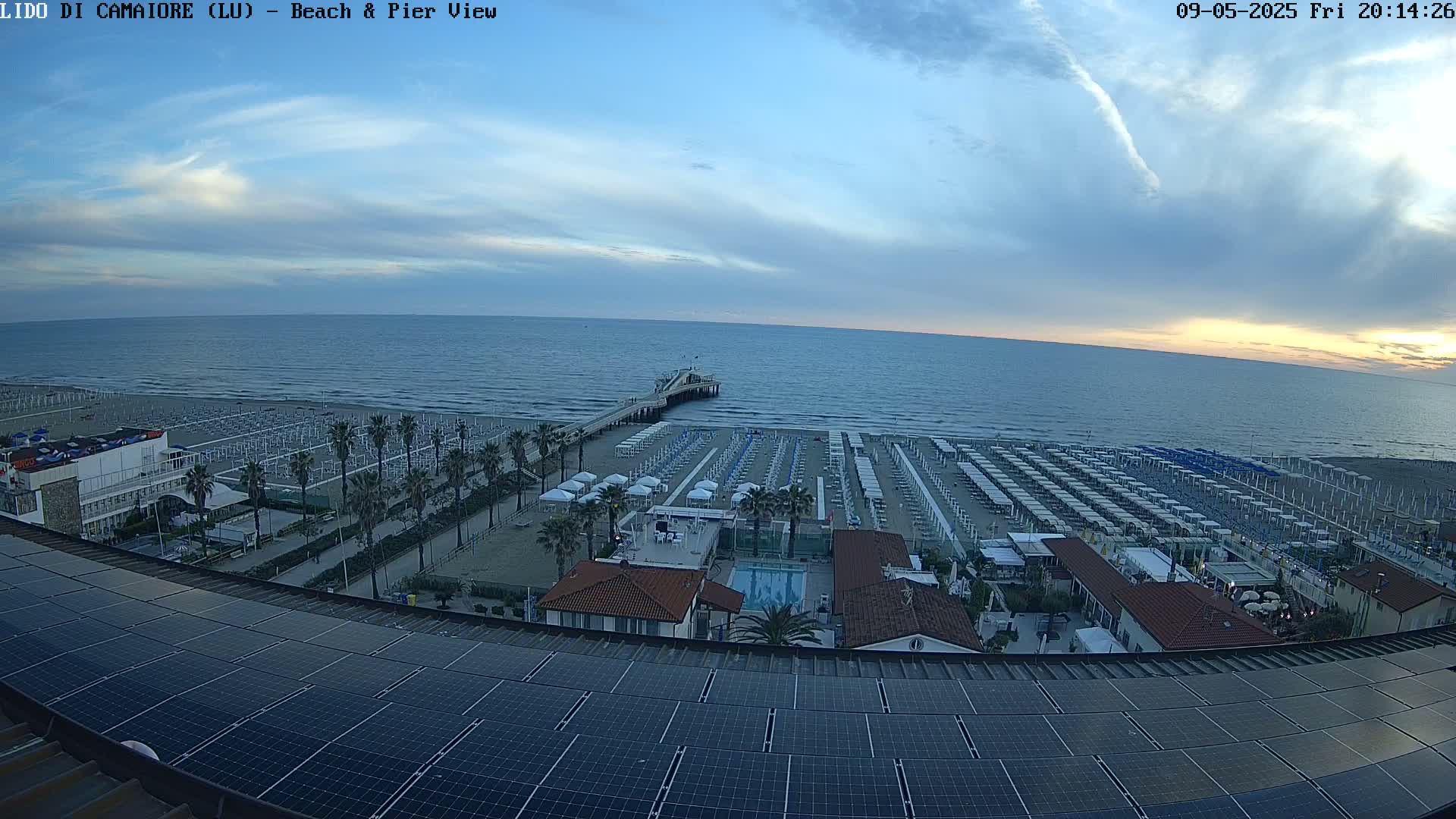 A beach with rows of umbrellas and a pier extends into a calm ocean under a twilight sky.