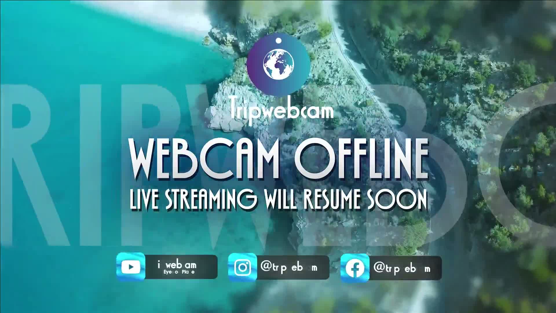 An aerial view of a coastline with clear turquoise water and green vegetation shows a webcam offline message.