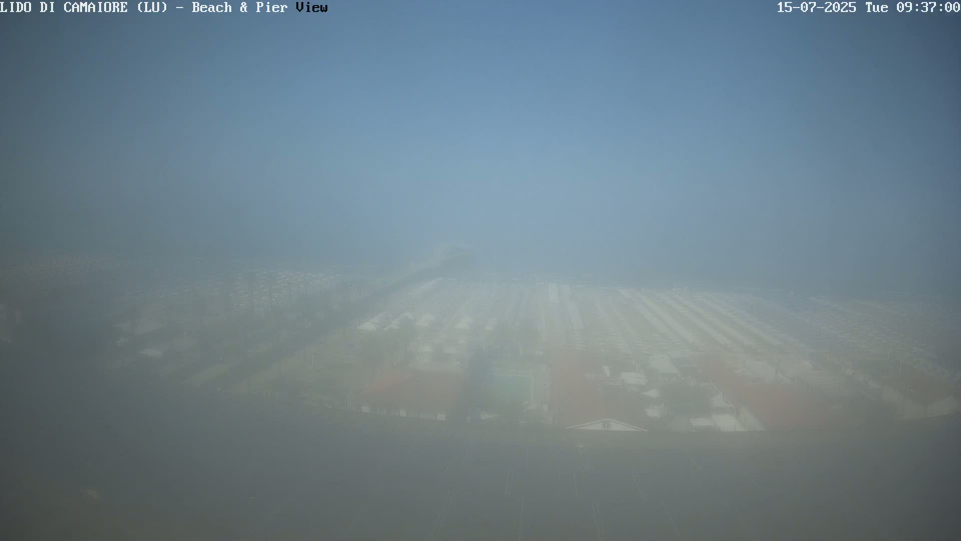 A hazy, foggy view shows a beach and pier area with many buildings barely visible in the distance.