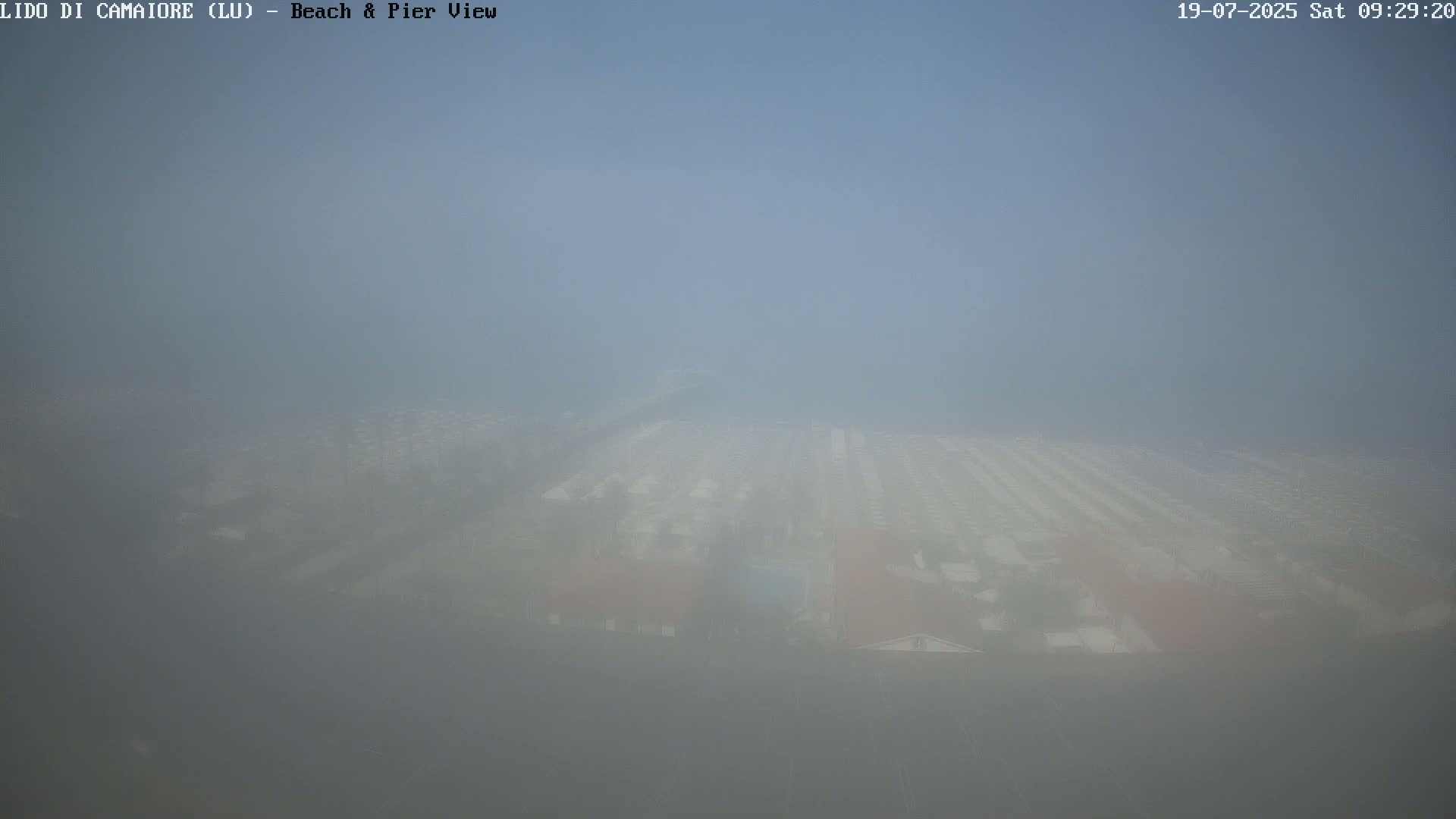 A hazy, foggy view of a beach and pier area, with buildings barely visible in the distance.