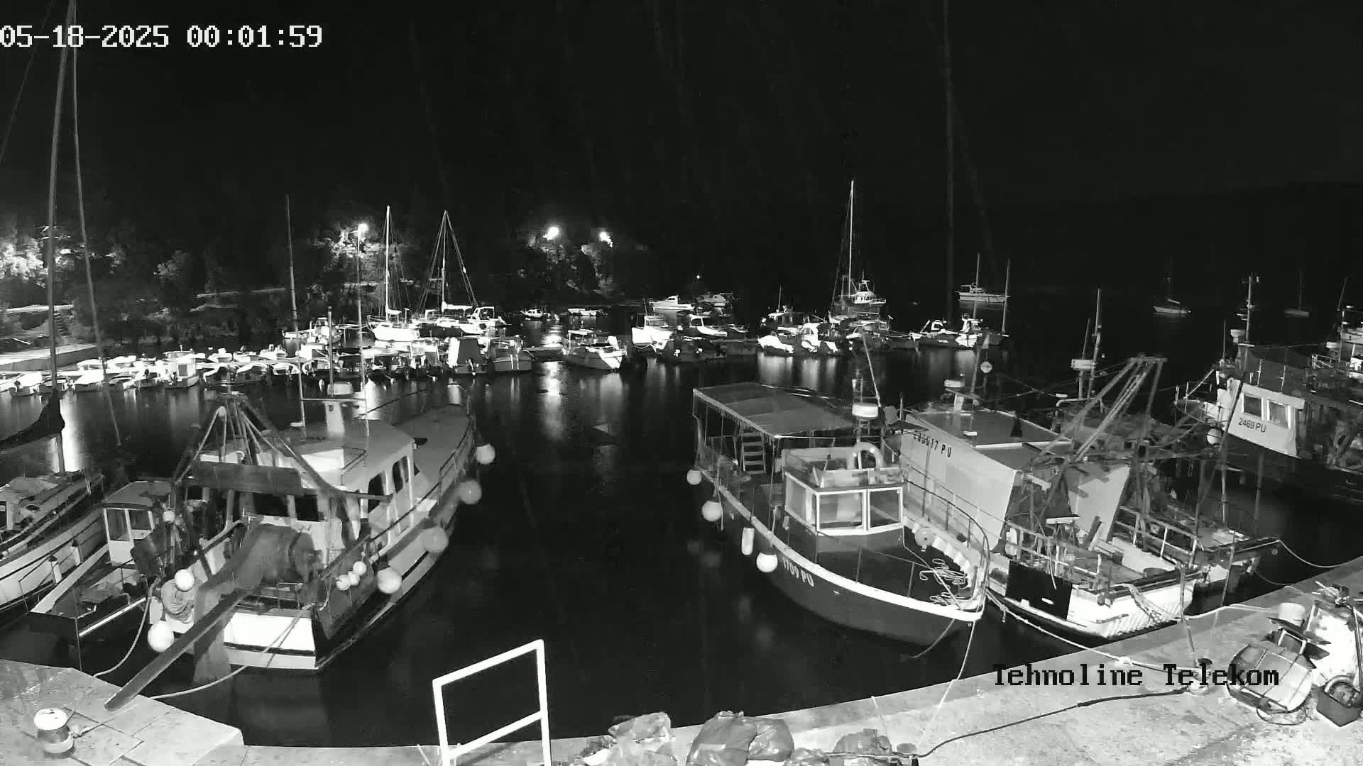 A nighttime, black and white view of a harbor filled with numerous boats and ships, mostly docked.