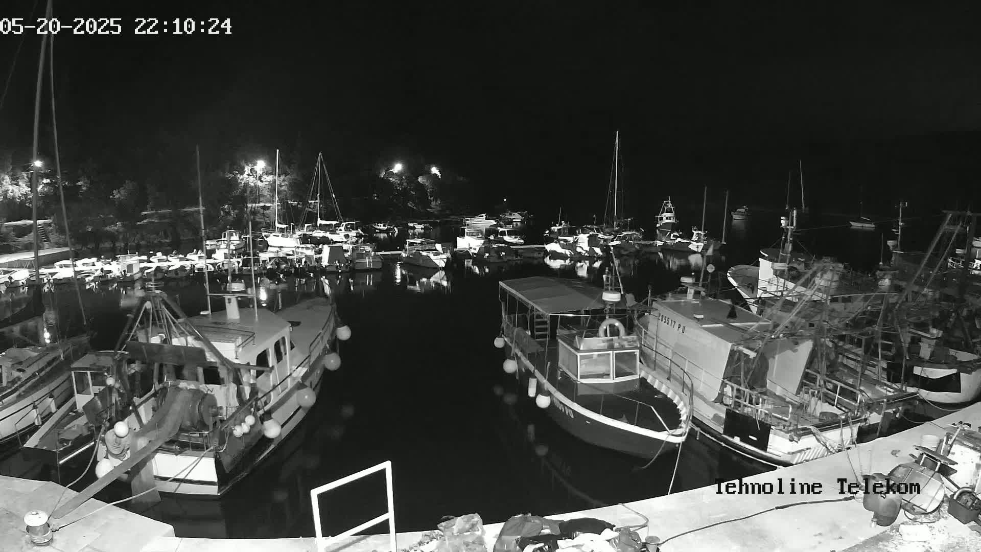 A nighttime, black-and-white view of a harbor filled with numerous boats and yachts moored alongside a dock.