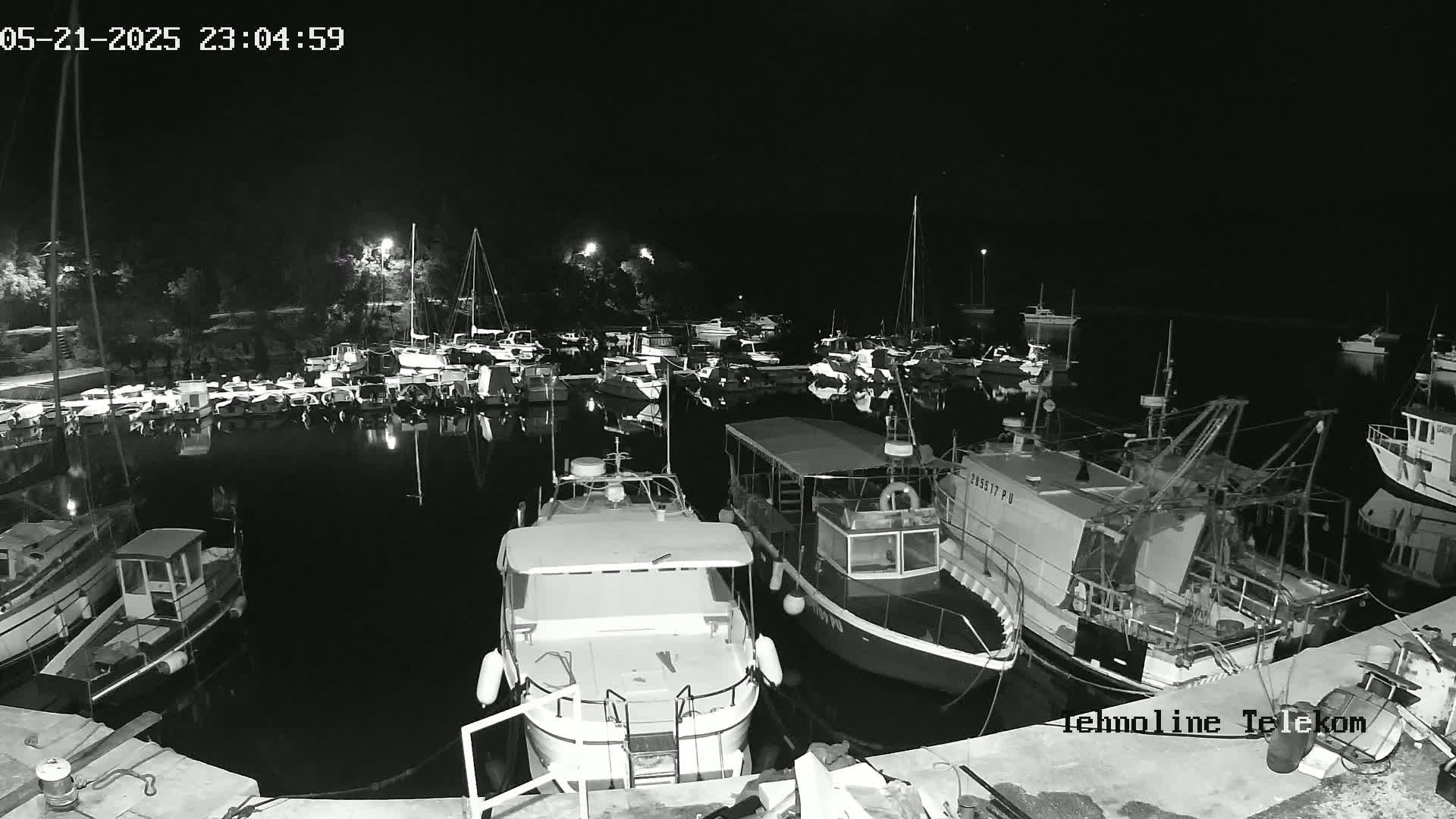A nighttime, black and white view of a harbor filled with numerous boats and yachts docked at the water's edge.